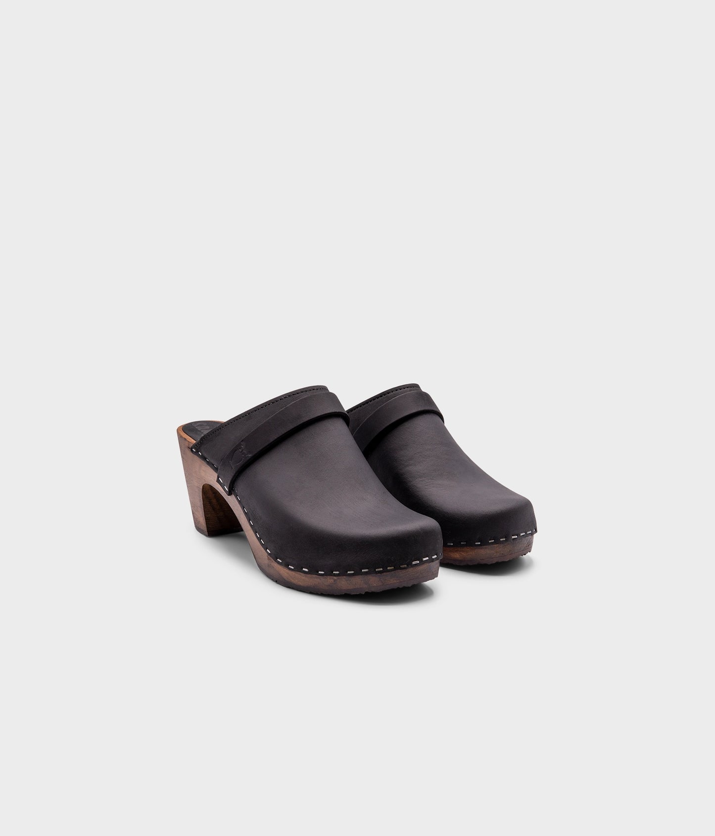 classic high rise heel clog mule in black nubuck leather stapled on a dark wooden base