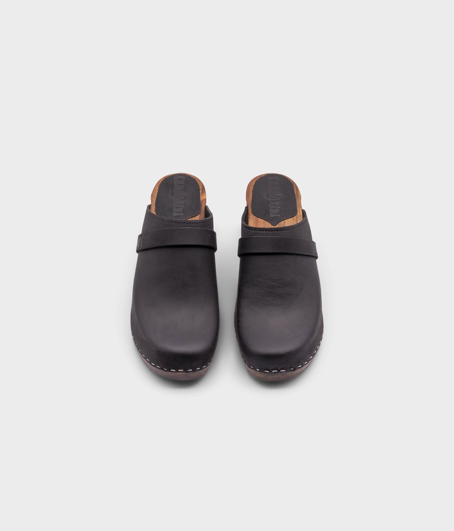classic high rise heel clog mule in black nubuck leather stapled on a dark wooden base