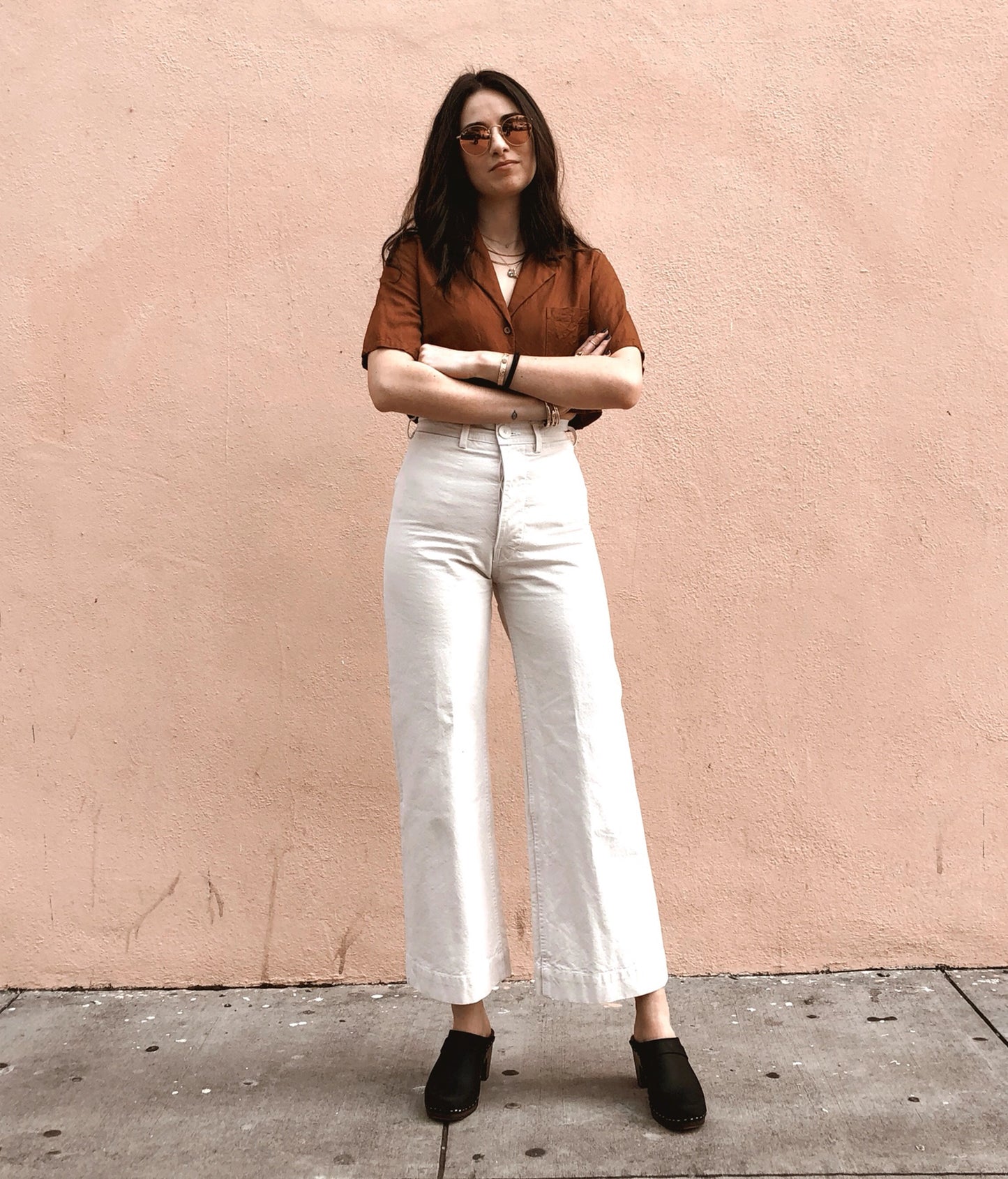 classic high rise heel clog mule in black nubuck leather stapled on a dark wooden base paired with white jeans and a brown button-down shirt