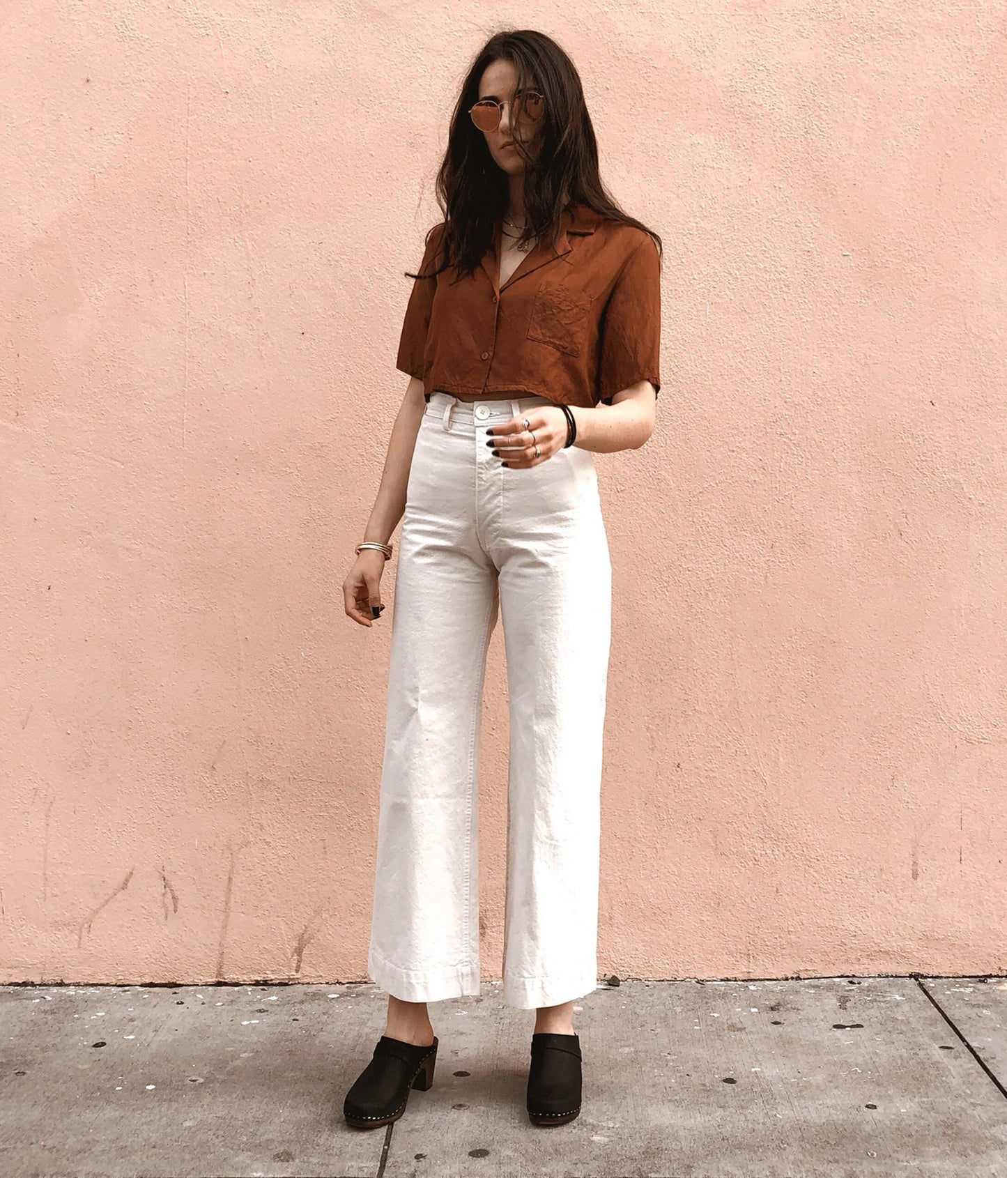 classic high rise heel clog mule in black nubuck leather stapled on a dark wooden base paired with white jeans and a brown button-down shirt