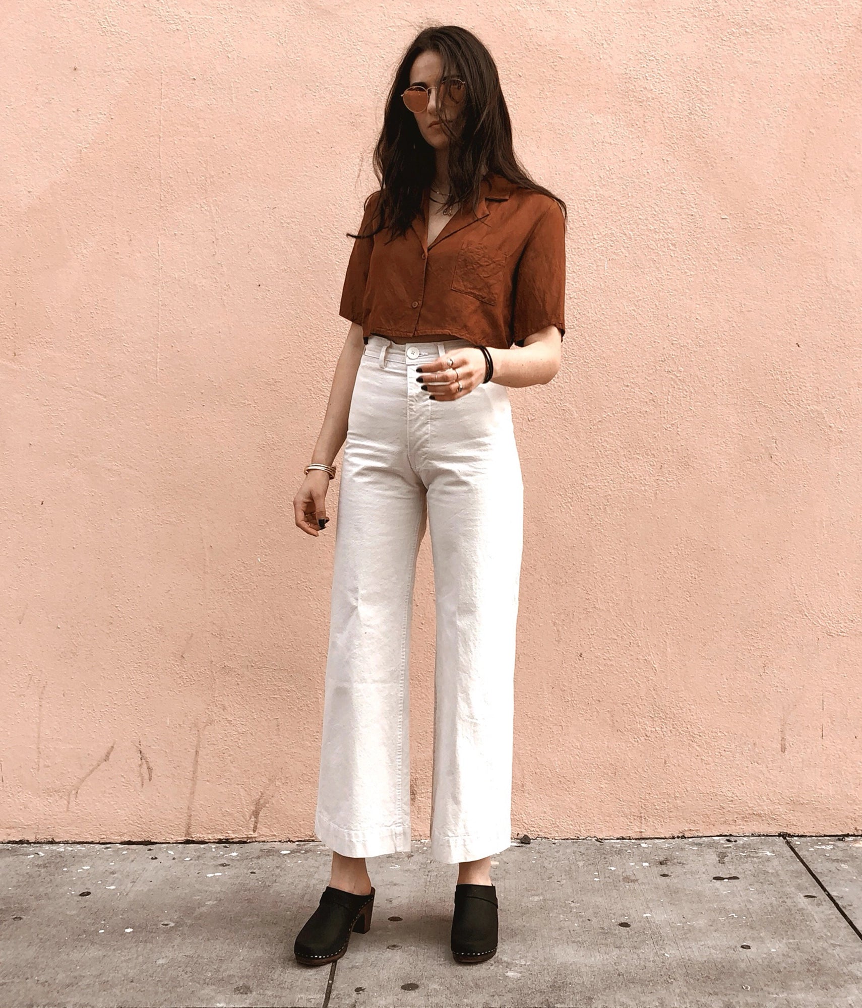 classic high rise heel clog mule in black nubuck leather stapled on a dark wooden base paired with white jeans and a brown button-down shirt