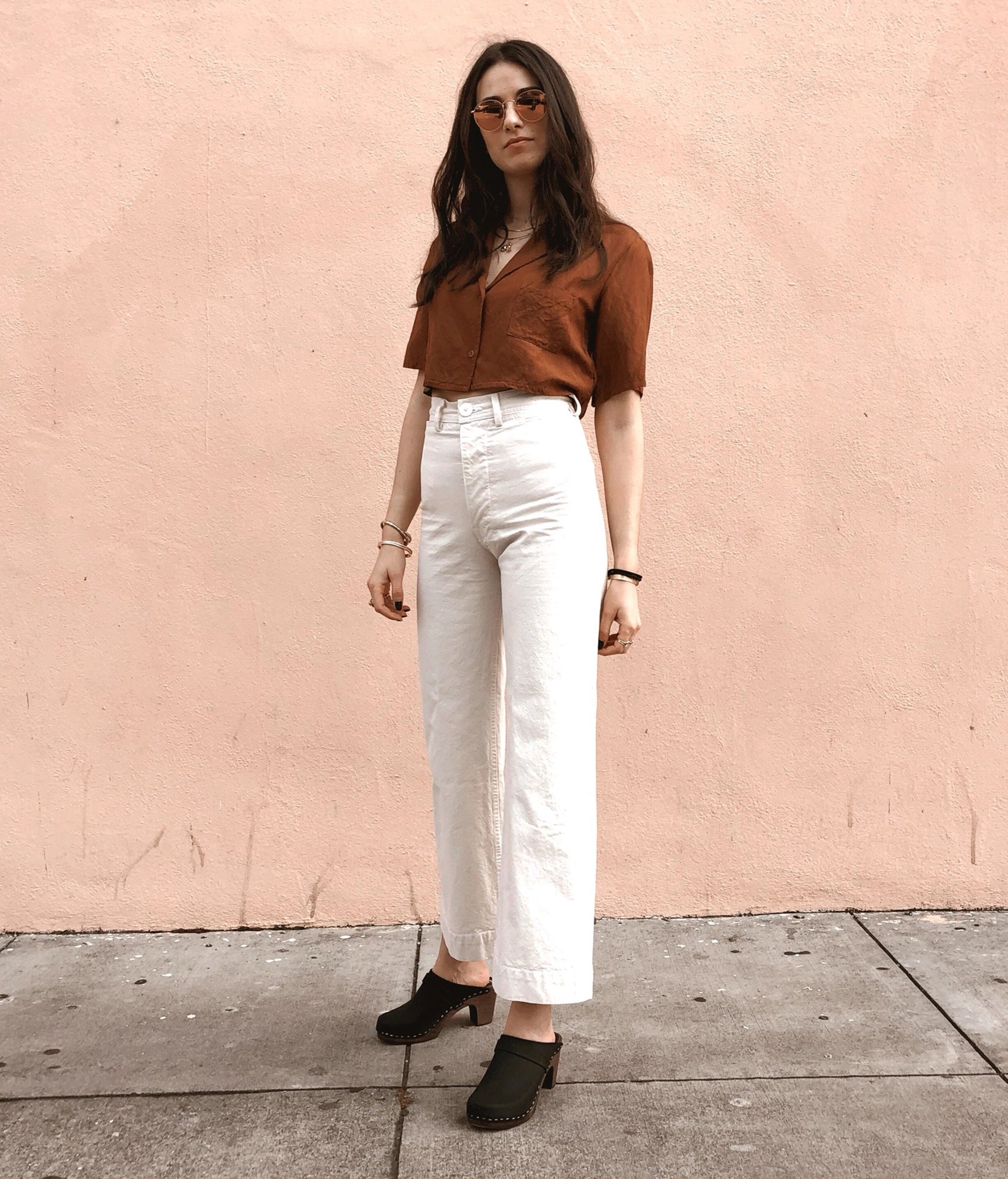 classic high rise heel clog mule in black nubuck leather stapled on a dark wooden base paired with white jeans and a brown button-down shirt