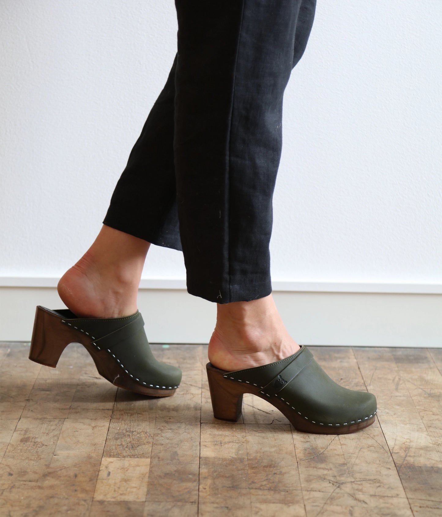 classic high rise heel clog mule in olive green nubuck leather stapled on a dark wooden base