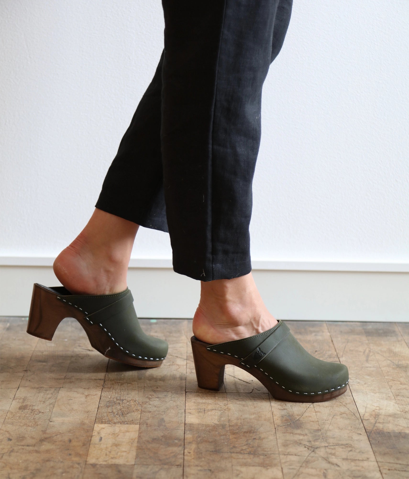 classic high rise heel clog mule in olive green nubuck leather stapled on a dark wooden base