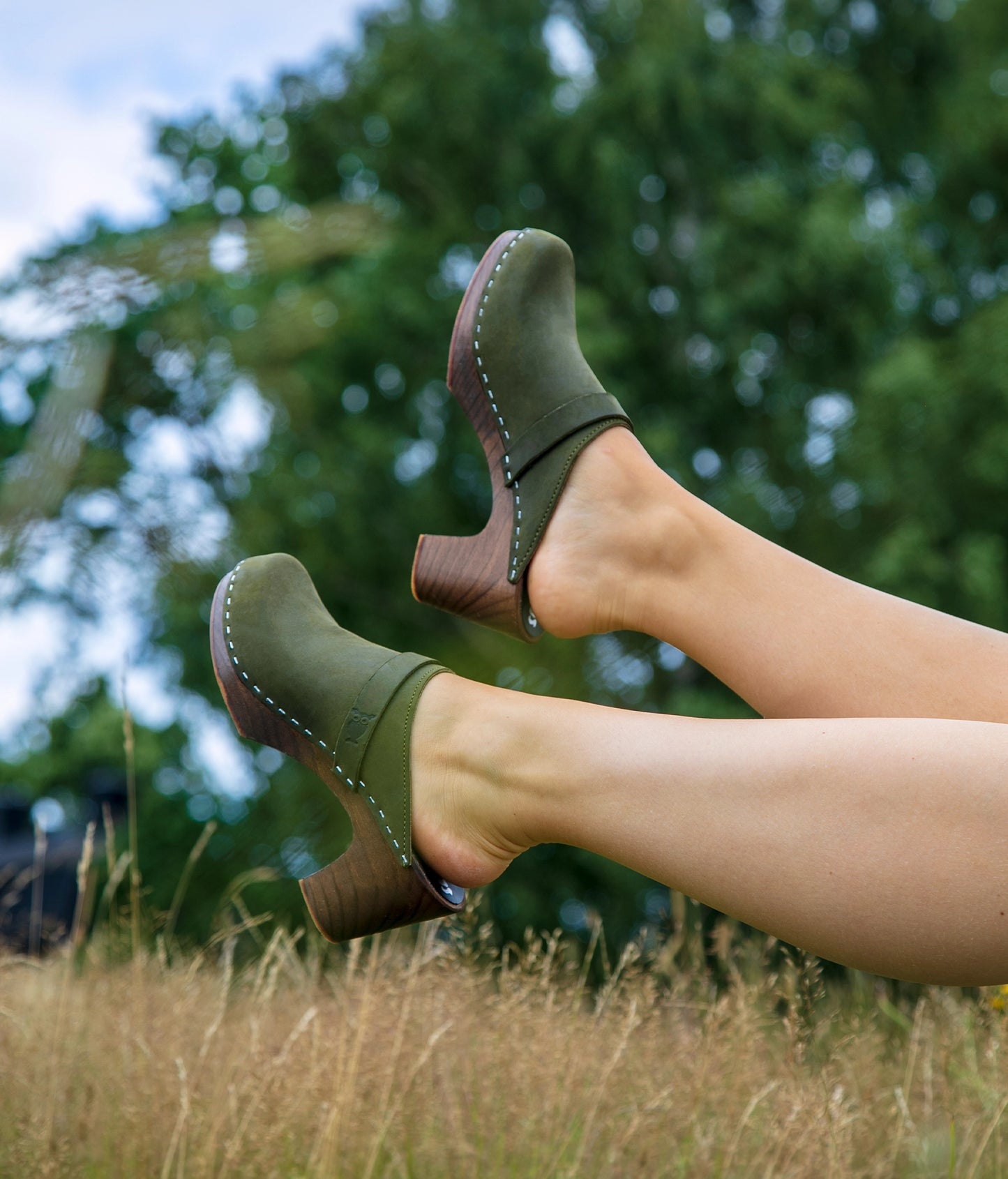 Pair of Olive colored clog mules with green background