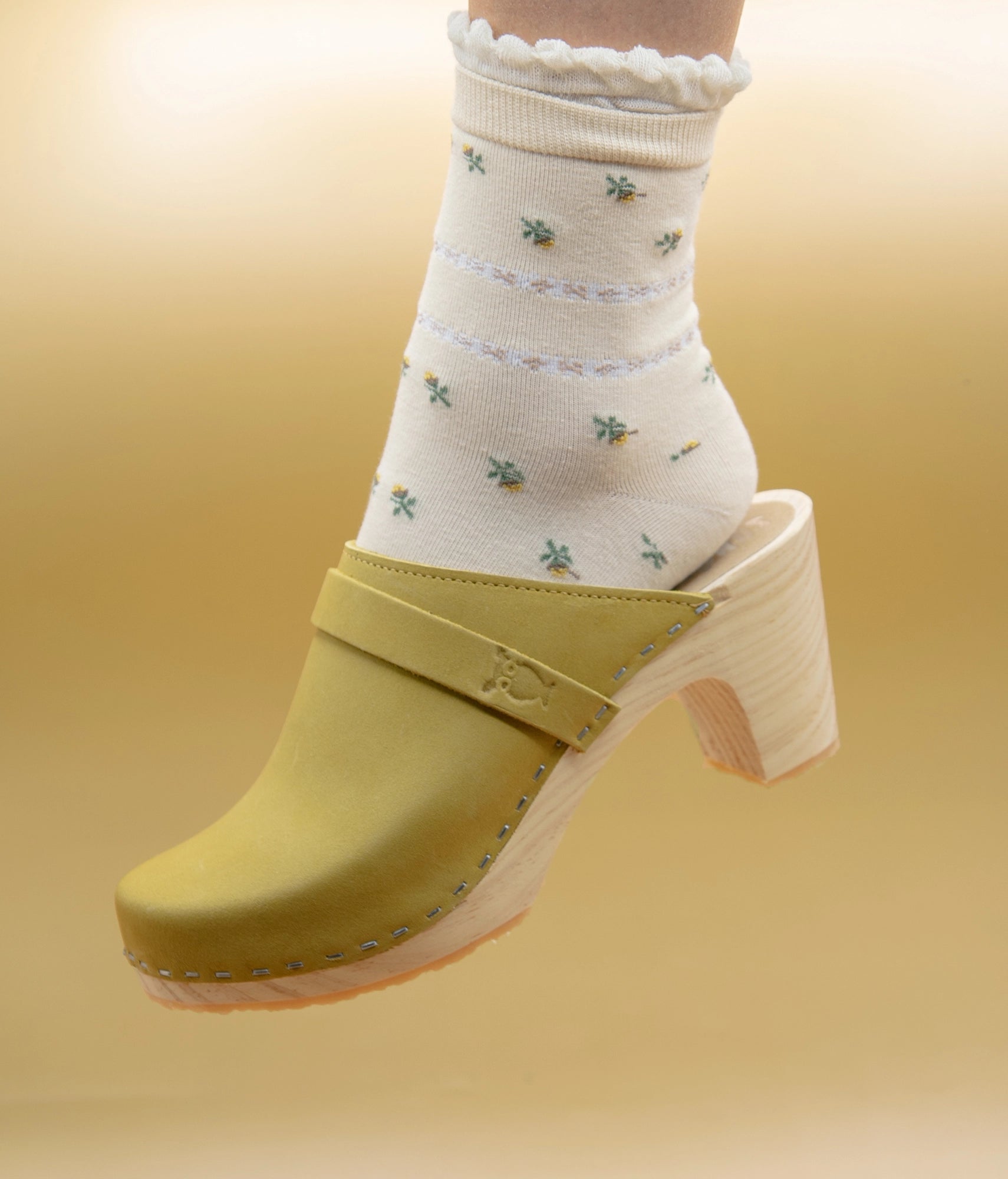 Yellow wooden clog mule worn with a white sock featuring floral patterns on a yellow background