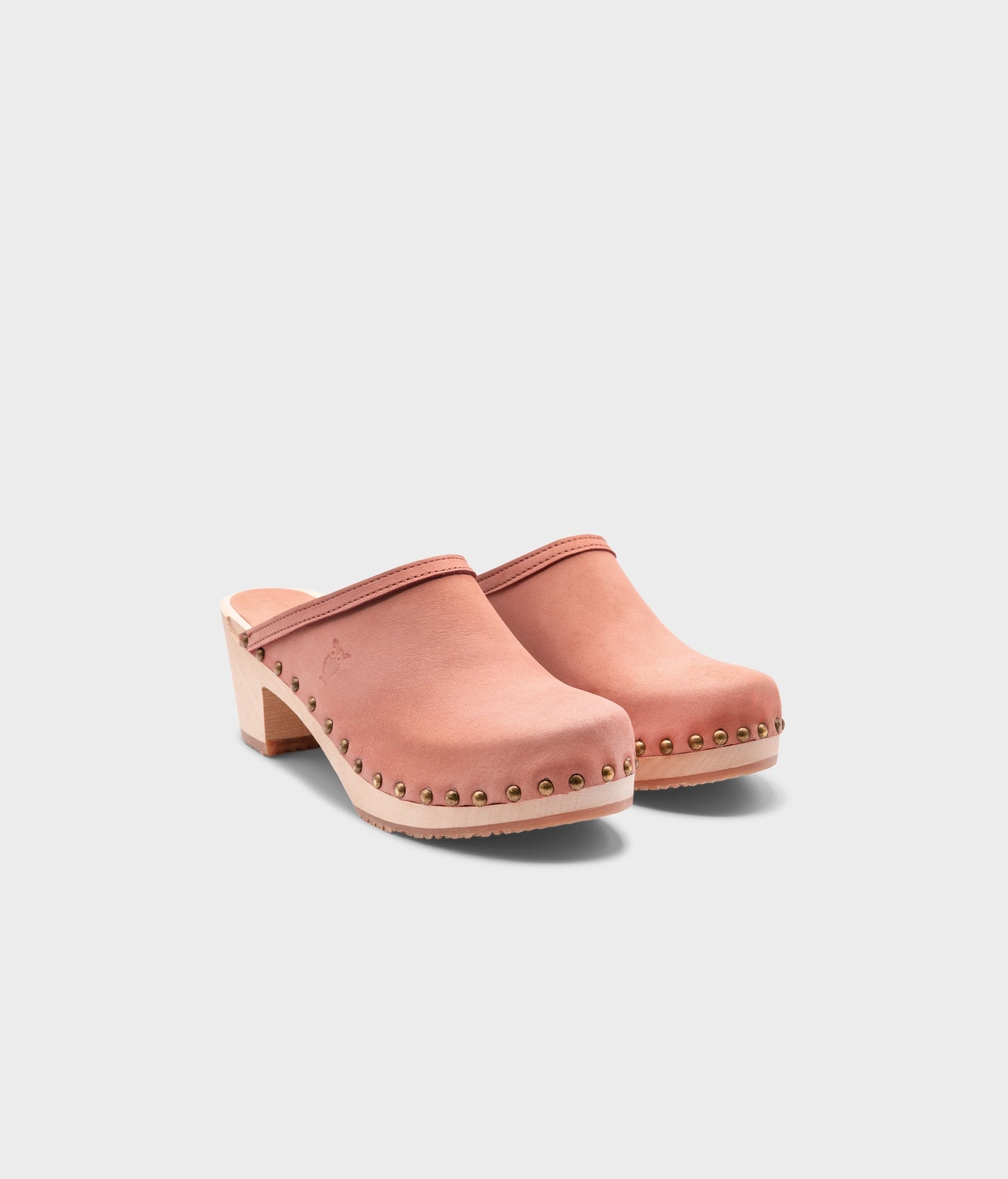 high heeled clog mules in blush pink nubuck leather stapled on a light wooden base with brass gold studs
