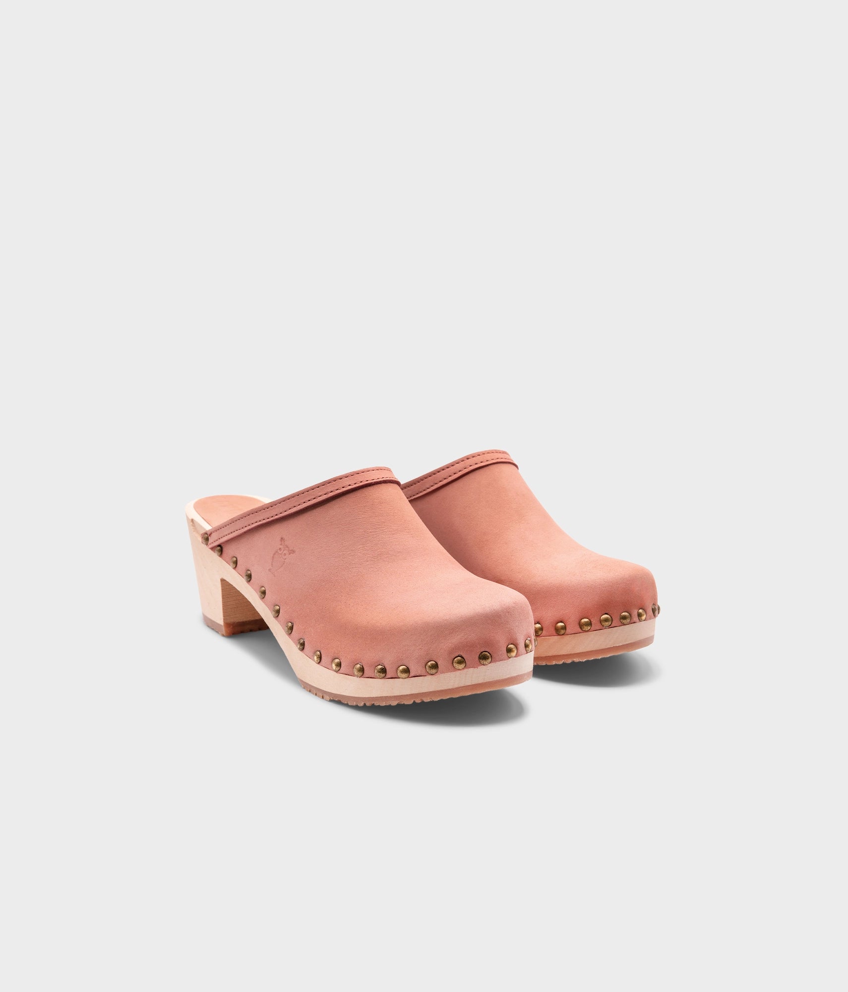 high heeled clog mules in blush pink nubuck leather stapled on a light wooden base with brass gold studs