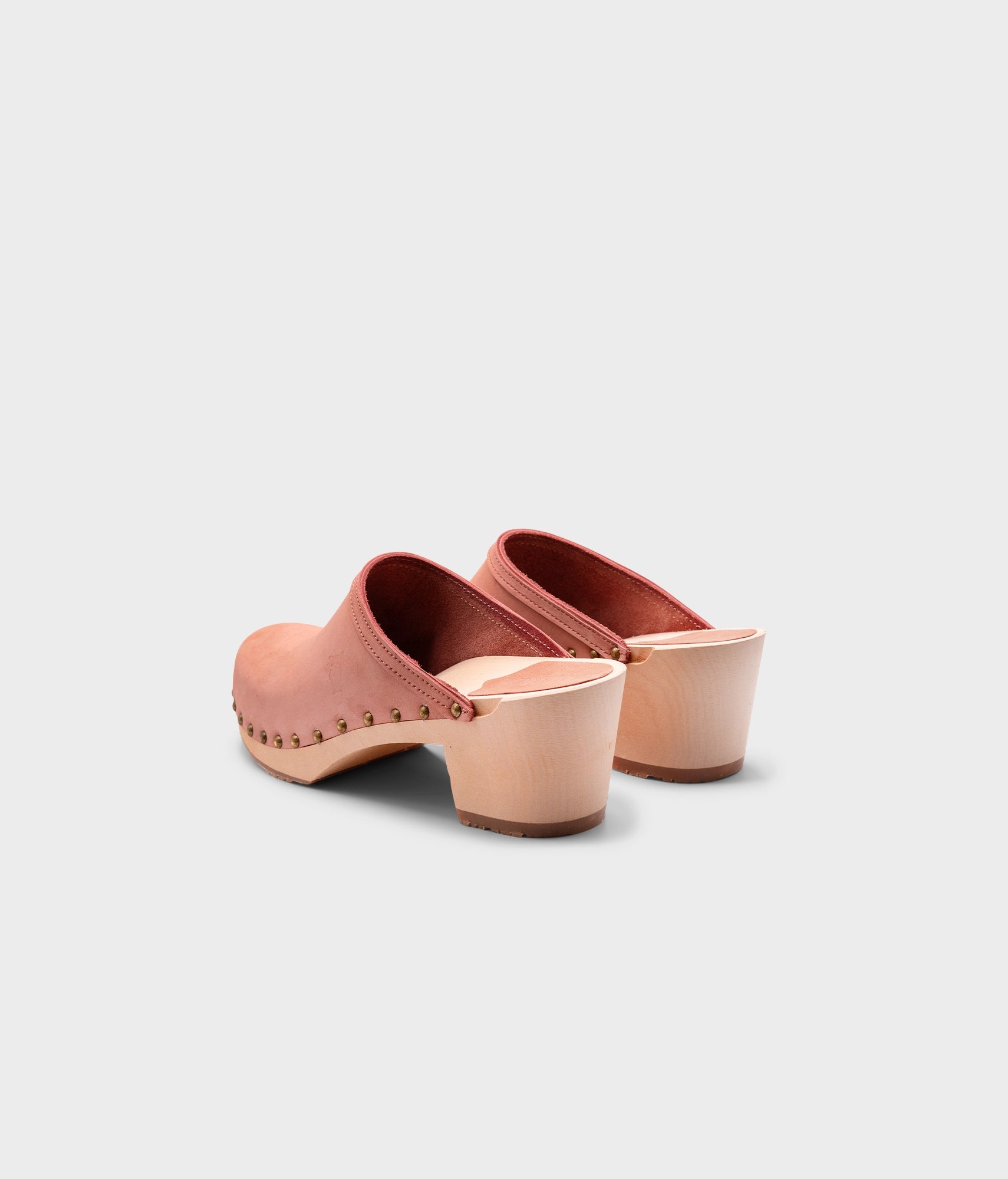 high heeled clog mules in blush pink nubuck leather stapled on a light wooden base with brass gold studs