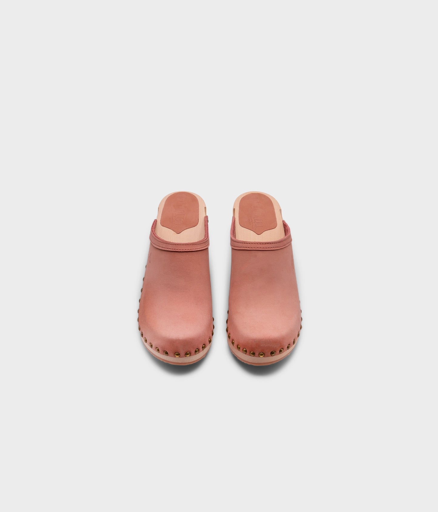 high heeled clog mules in blush pink nubuck leather stapled on a light wooden base with brass gold studs