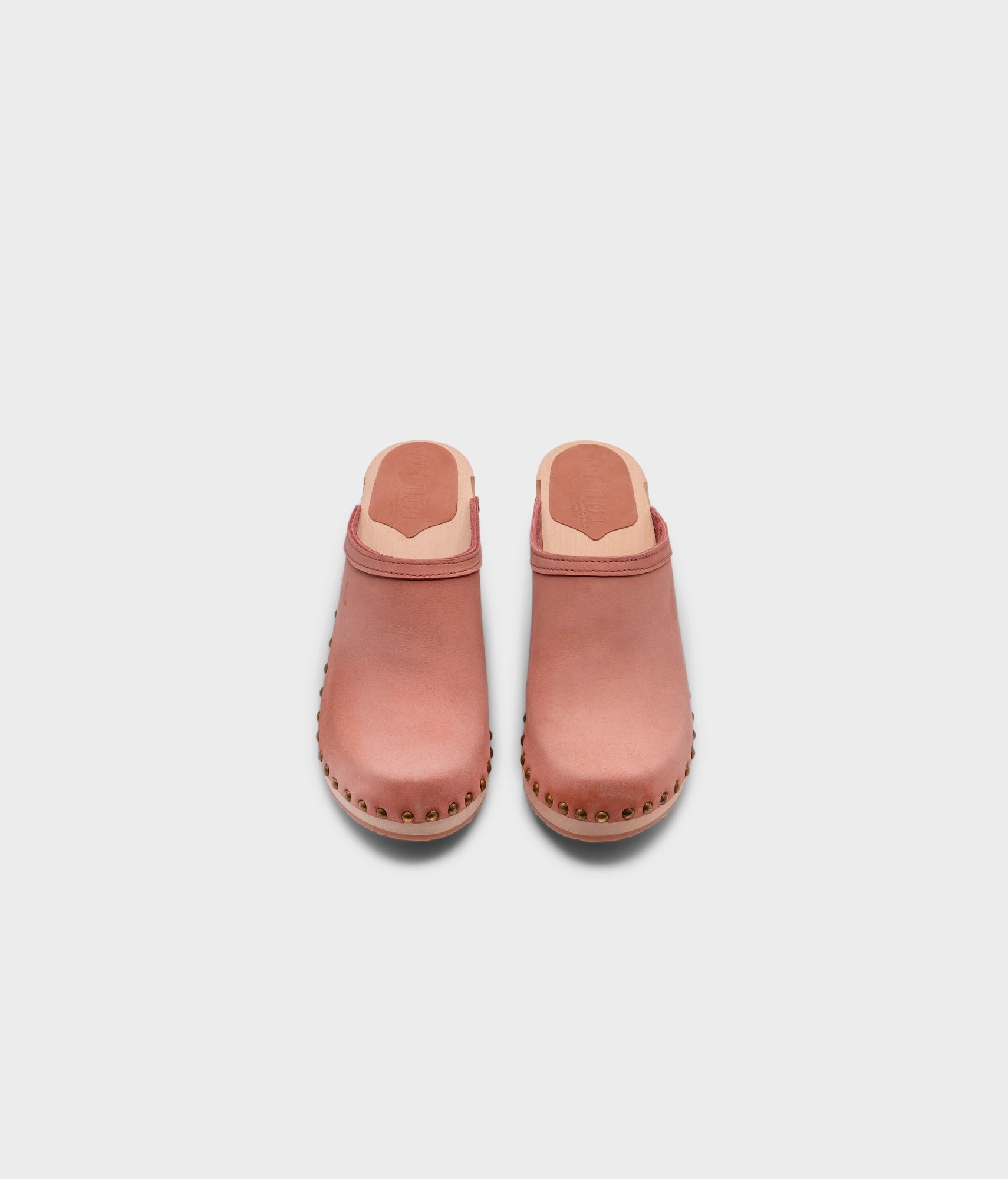 high heeled clog mules in blush pink nubuck leather stapled on a light wooden base with brass gold studs