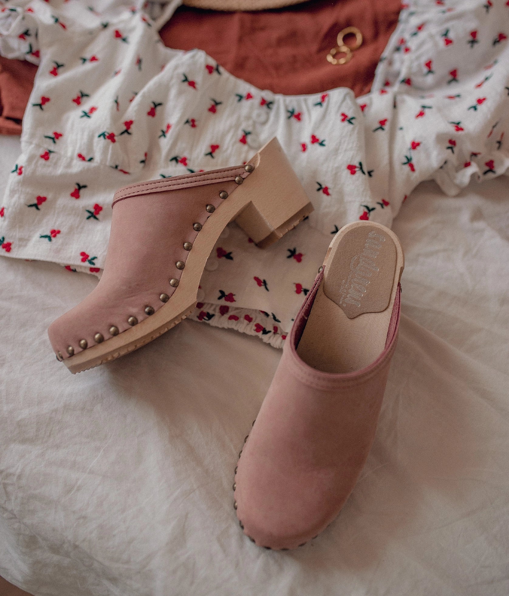 high heeled clog mules in blush pink nubuck leather stapled on a light wooden base with brass gold studs