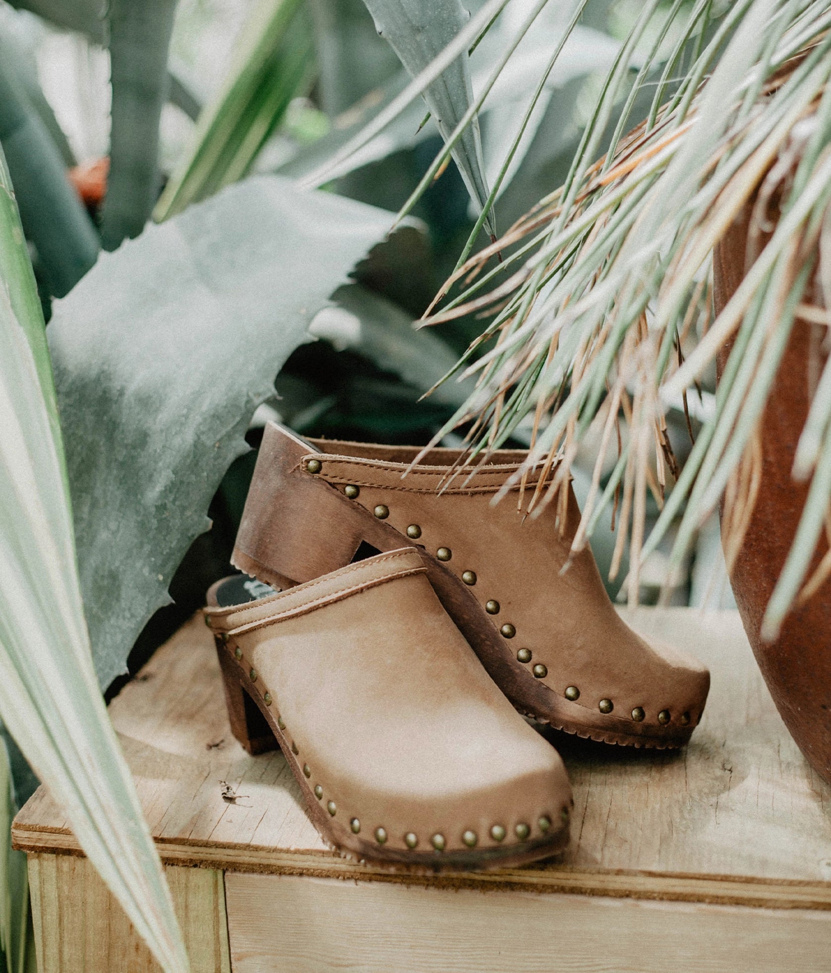 high heeled clog mules in light brown nubuck leather stapled on a dark wooden base with brass gold studs