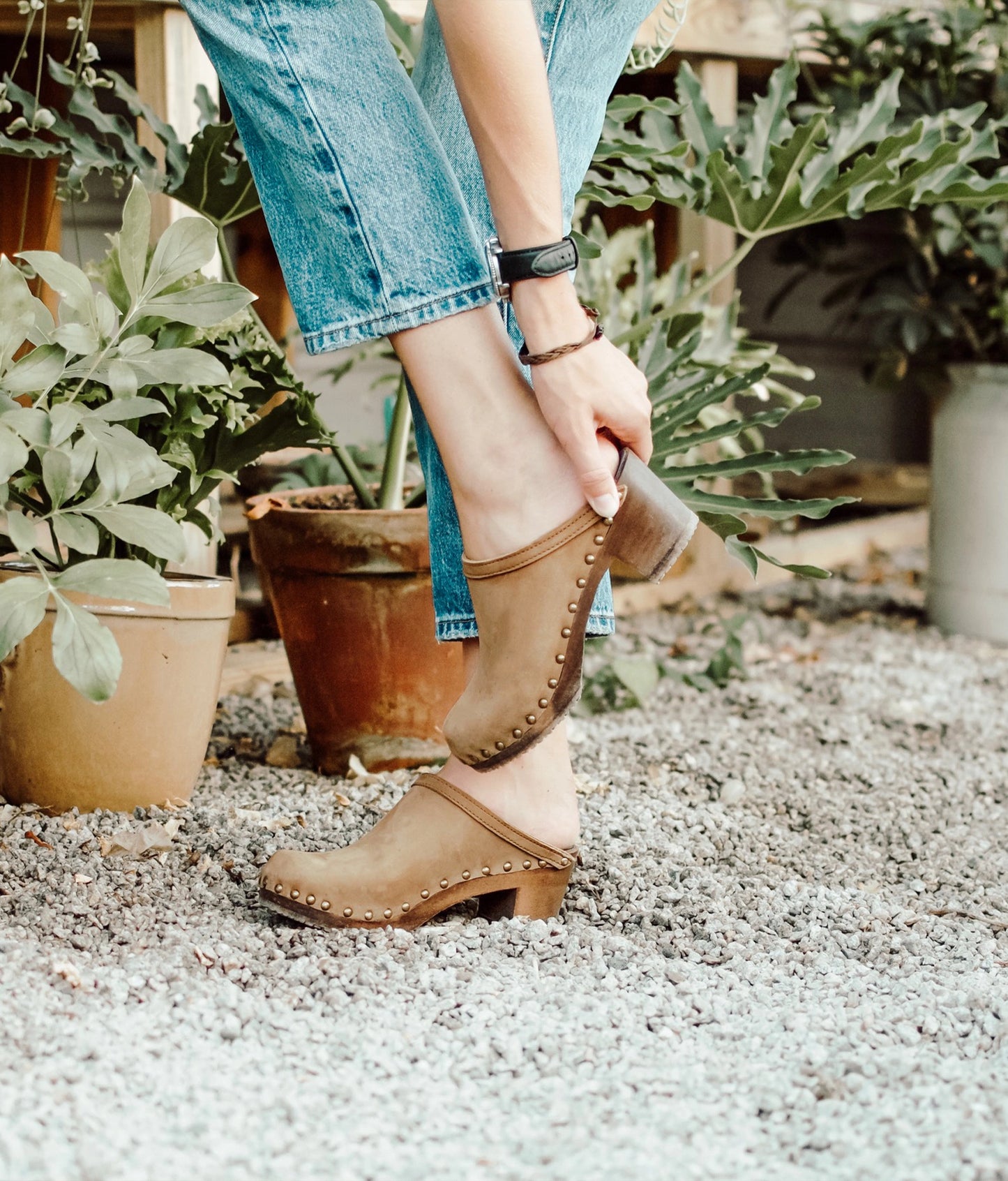 high heeled clog mules in light brown nubuck leather stapled on a dark wooden base with brass gold studs