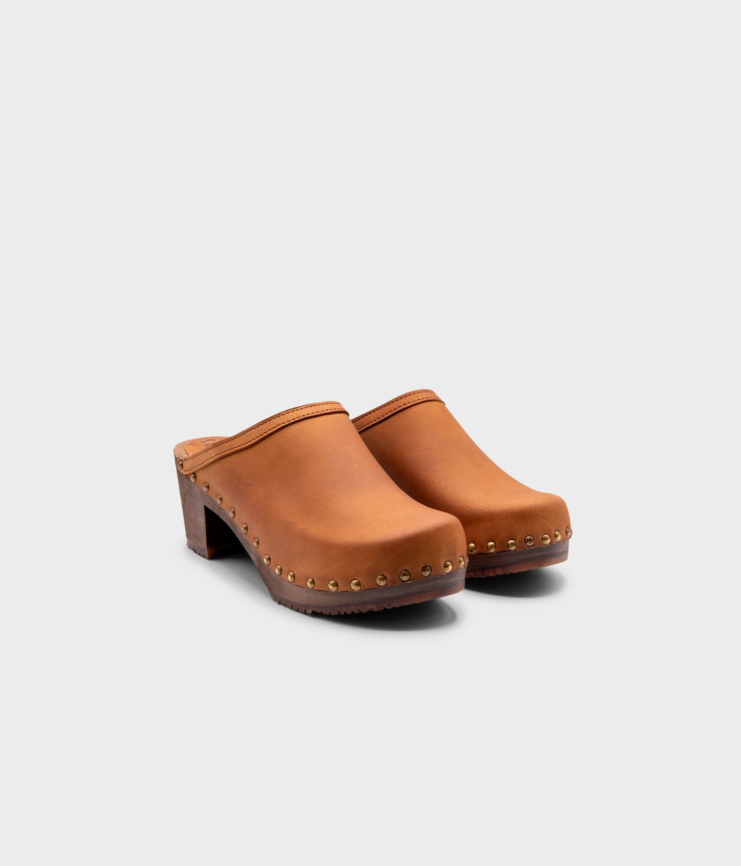 high heeled clog mules in light brown nubuck leather stapled on a dark wooden base with brass gold studs