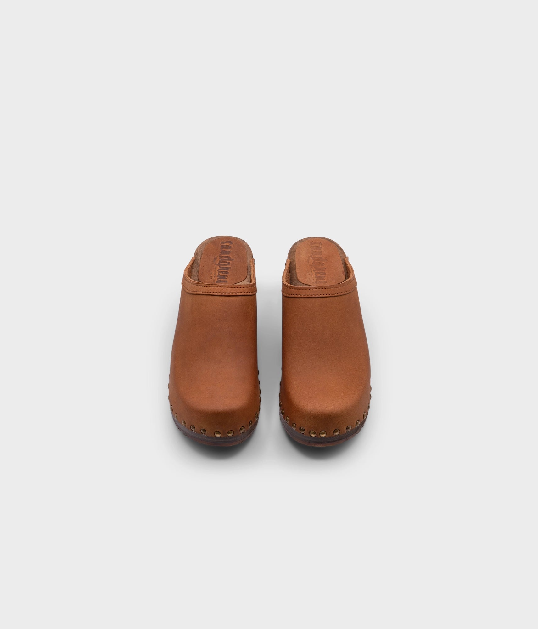 high heeled clog mules in light brown nubuck leather stapled on a dark wooden base with brass gold studs