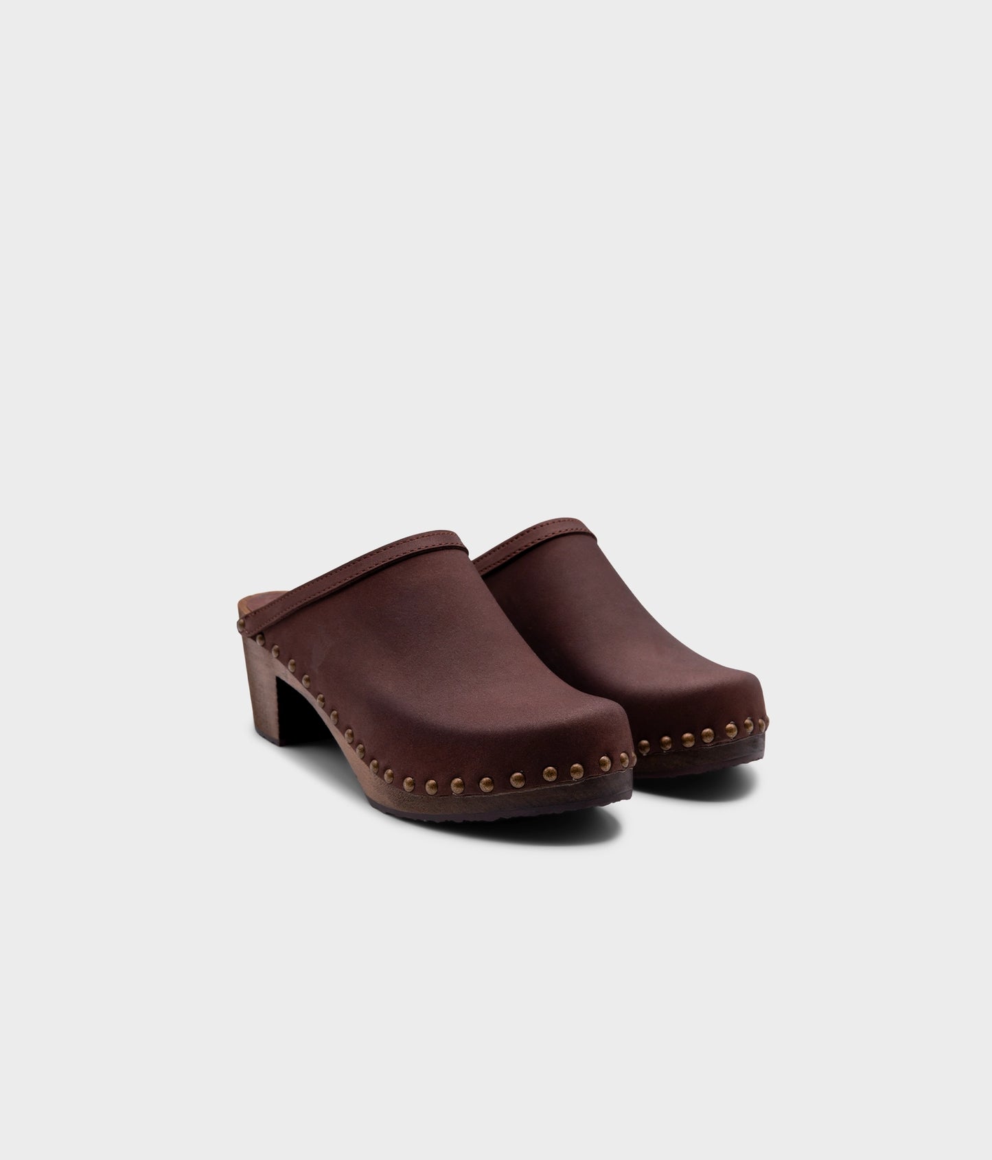 high heeled clog mules in dark brown nubuck leather stapled on a dark wooden base with brass gold studs