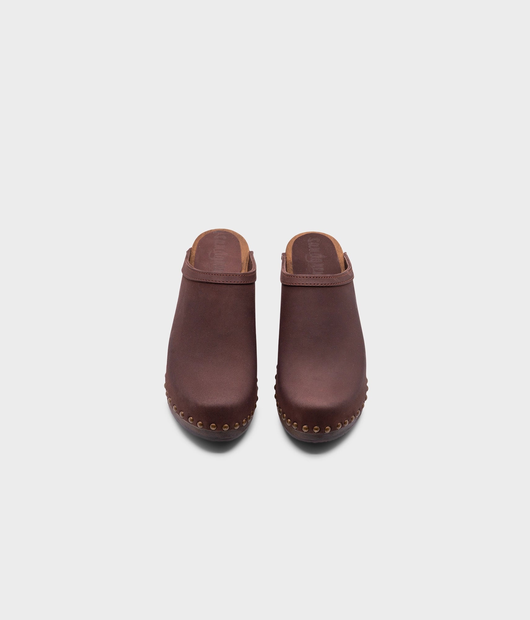 high heeled clog mules in dark brown nubuck leather stapled on a dark wooden base with brass gold studs