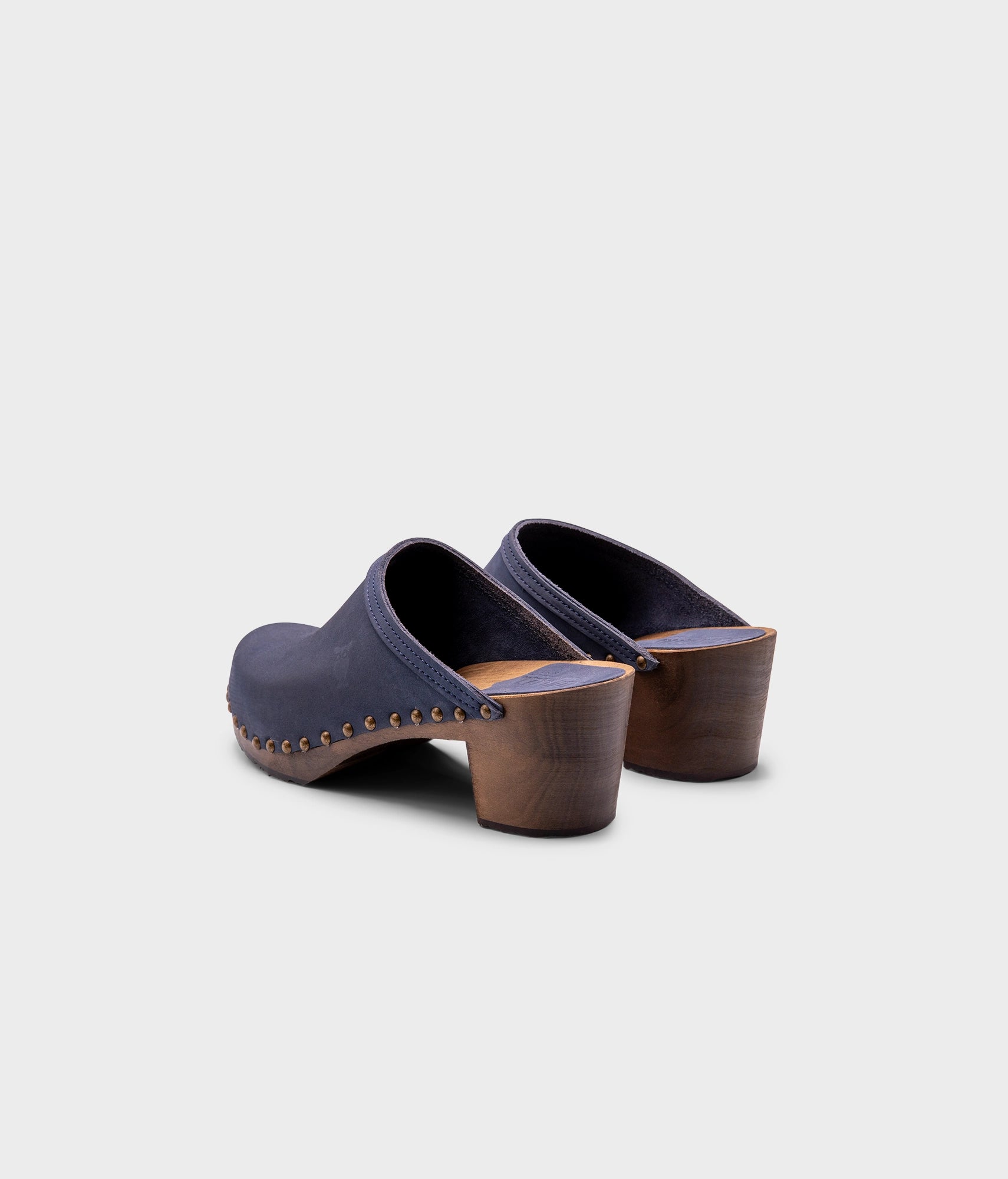 high heeled clog mules in navy blue nubuck leather stapled on a dark wooden base with brass gold studs