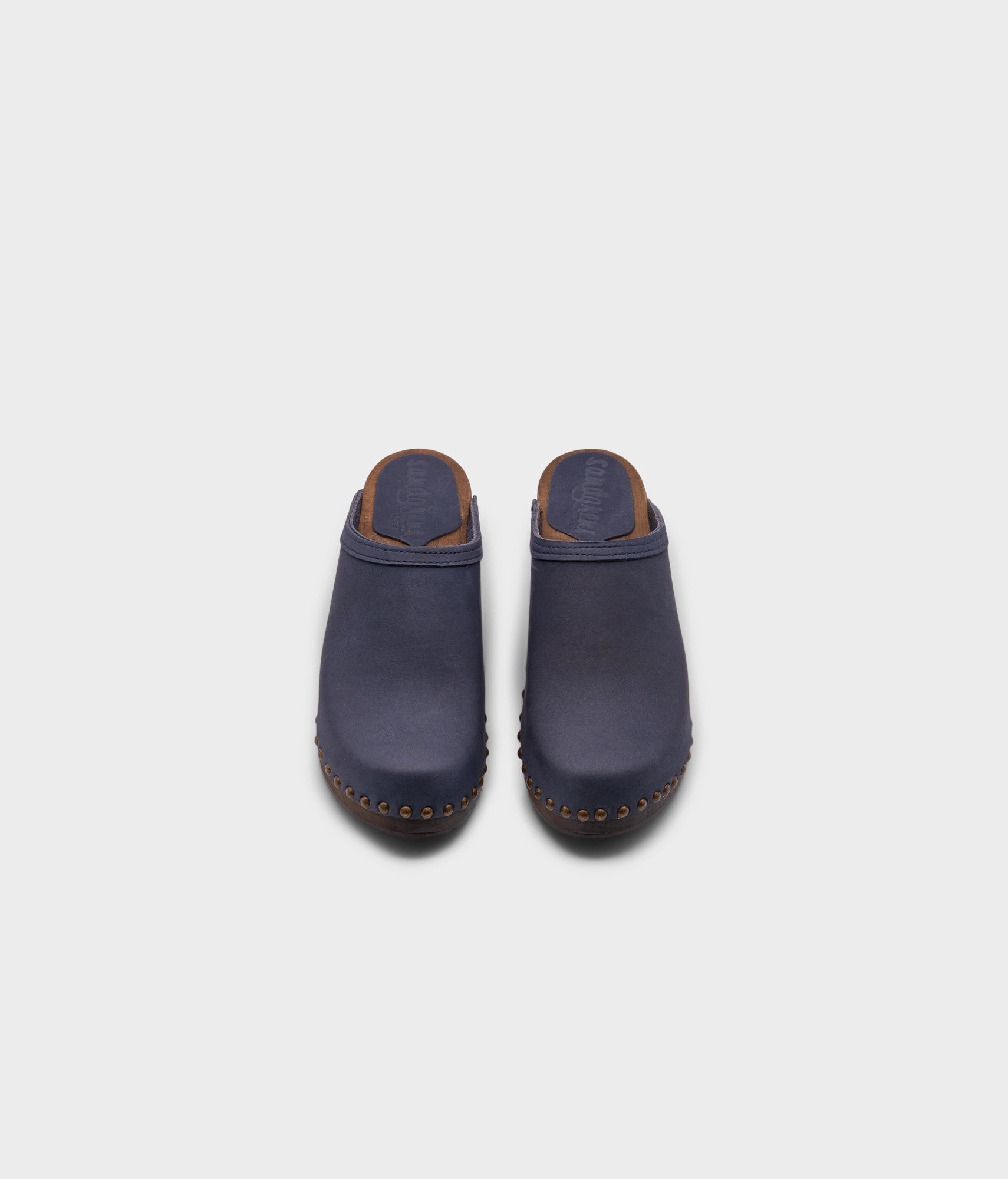 high heeled clog mules in navy blue nubuck leather stapled on a dark wooden base with brass gold studs