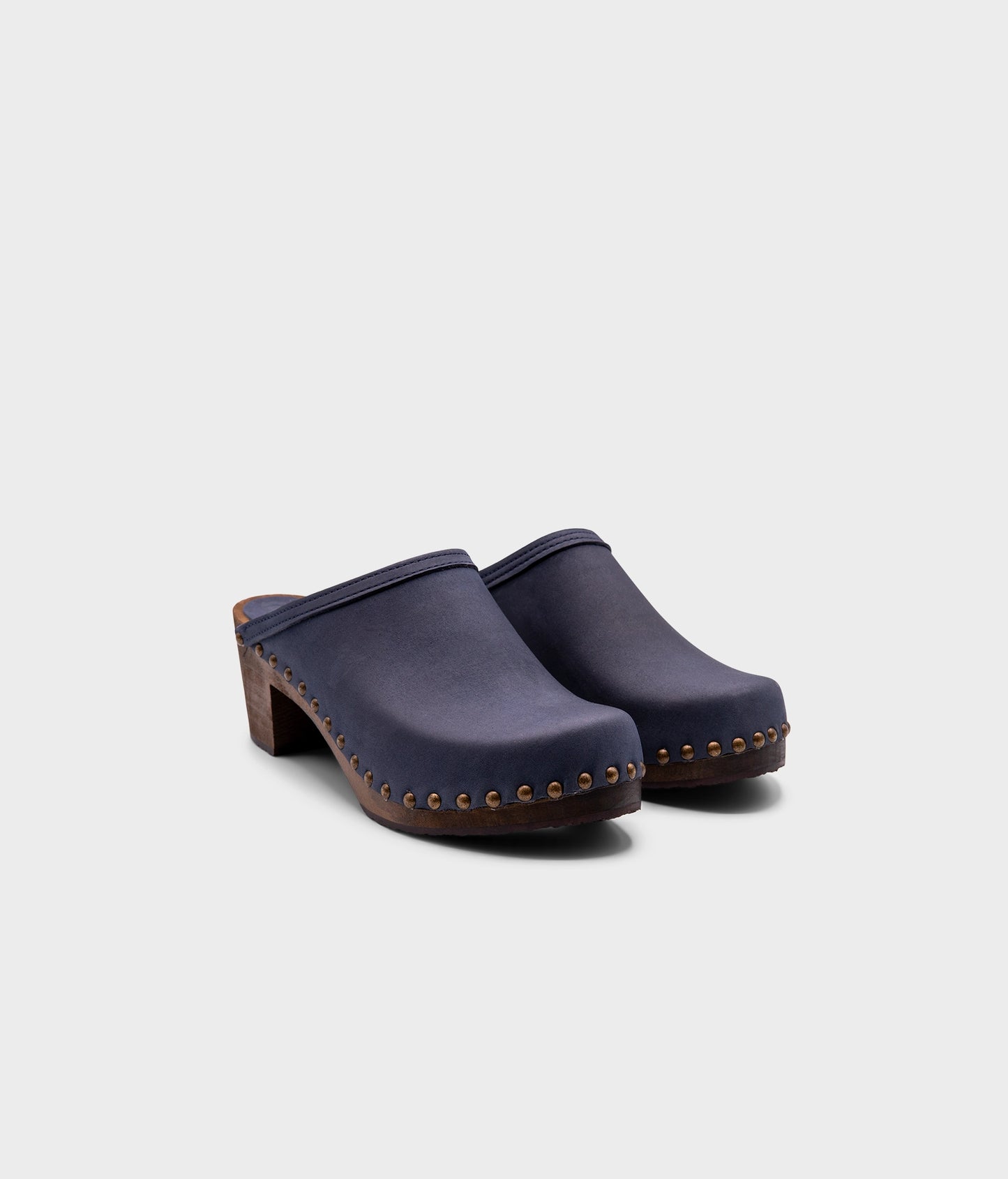 high heeled clog mules in navy blue nubuck leather stapled on a dark wooden base with brass gold studs