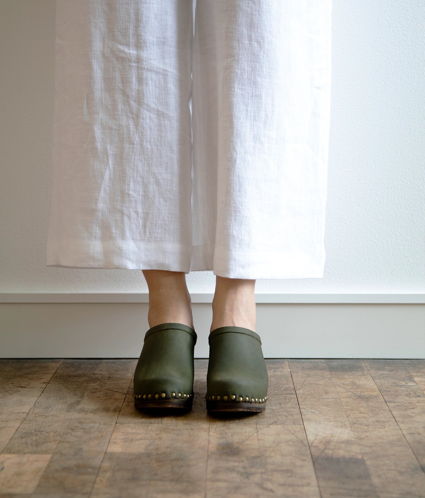 high heeled clog mules in olive green nubuck leather stapled on a dark wooden base with brass gold studs