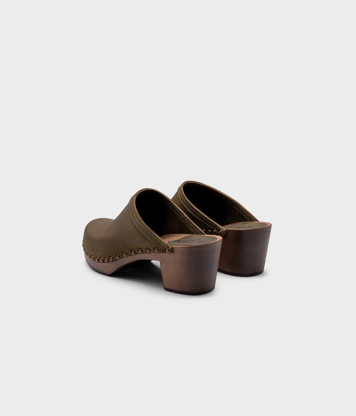 high heeled clog mules in olive green nubuck leather stapled on a dark wooden base with brass gold studs