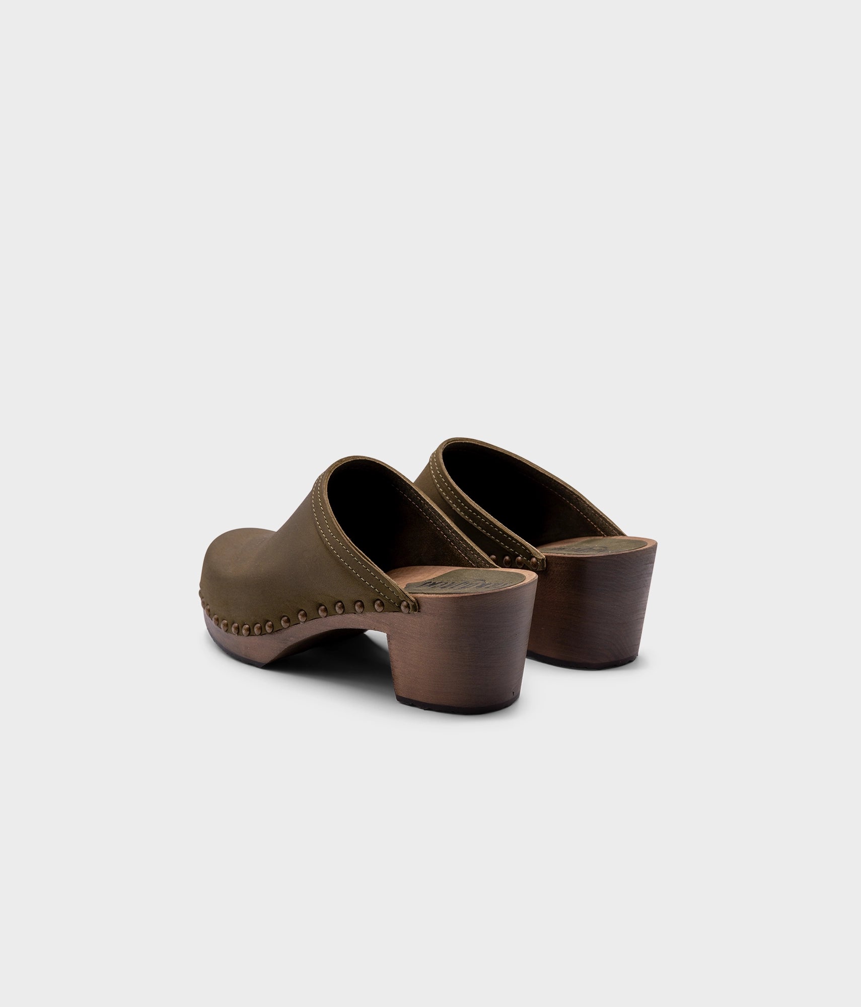 high heeled clog mules in olive green nubuck leather stapled on a dark wooden base with brass gold studs