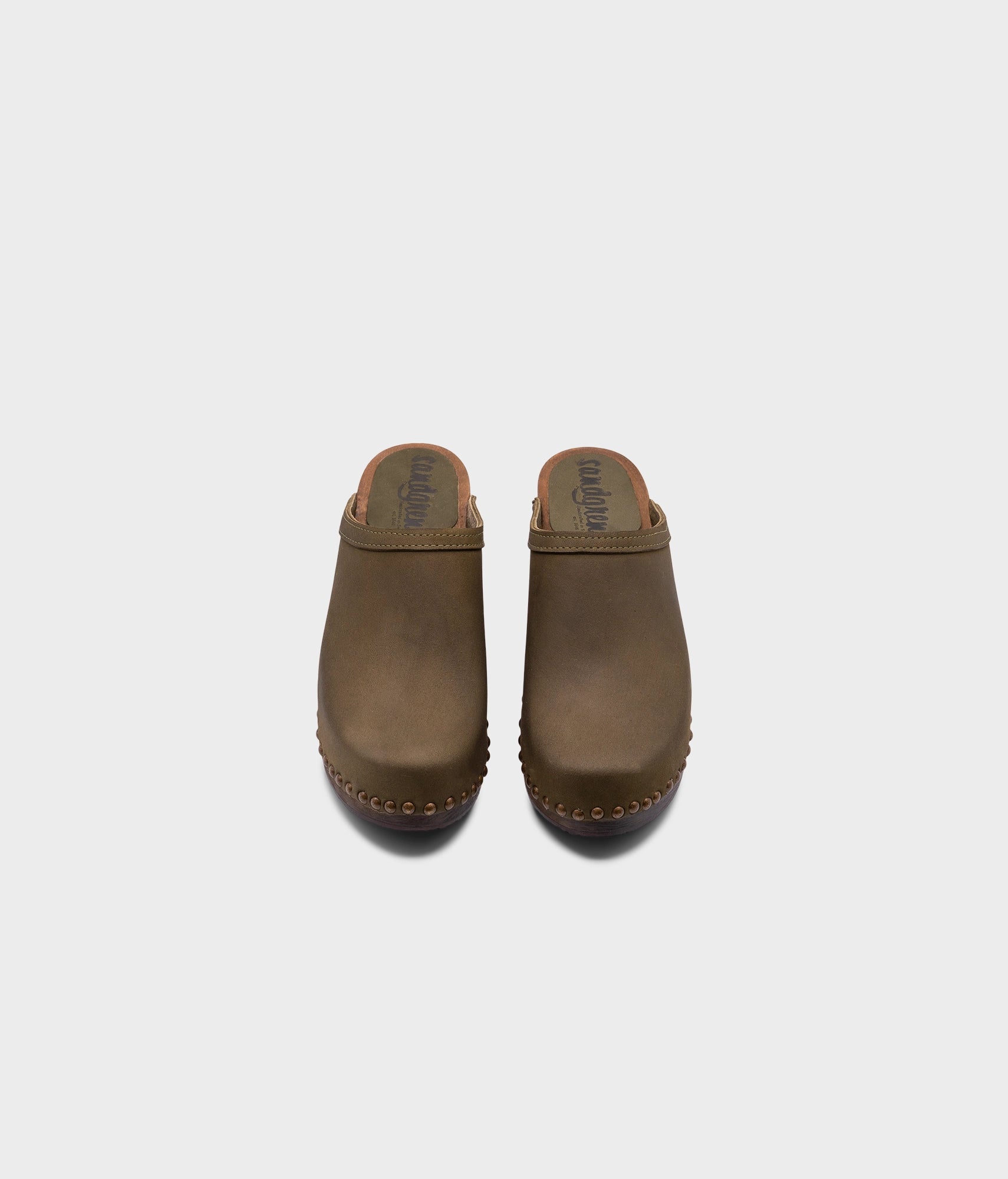 high heeled clog mules in olive green nubuck leather stapled on a dark wooden base with brass gold studs