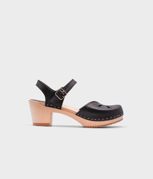 high-heeled clog sandal in black vegetable tanned leather with a blossom cut-out over the toe stapled on a light wooden base