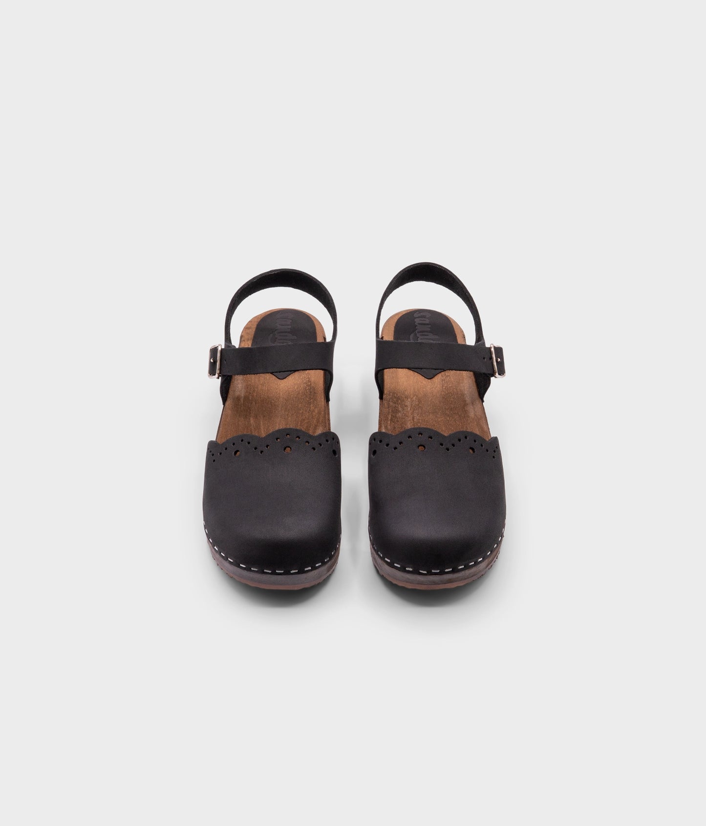 low heeled closed-toe clog sandals in black nubuck leather with a wavy leather cutout stapled on a dark wooden base