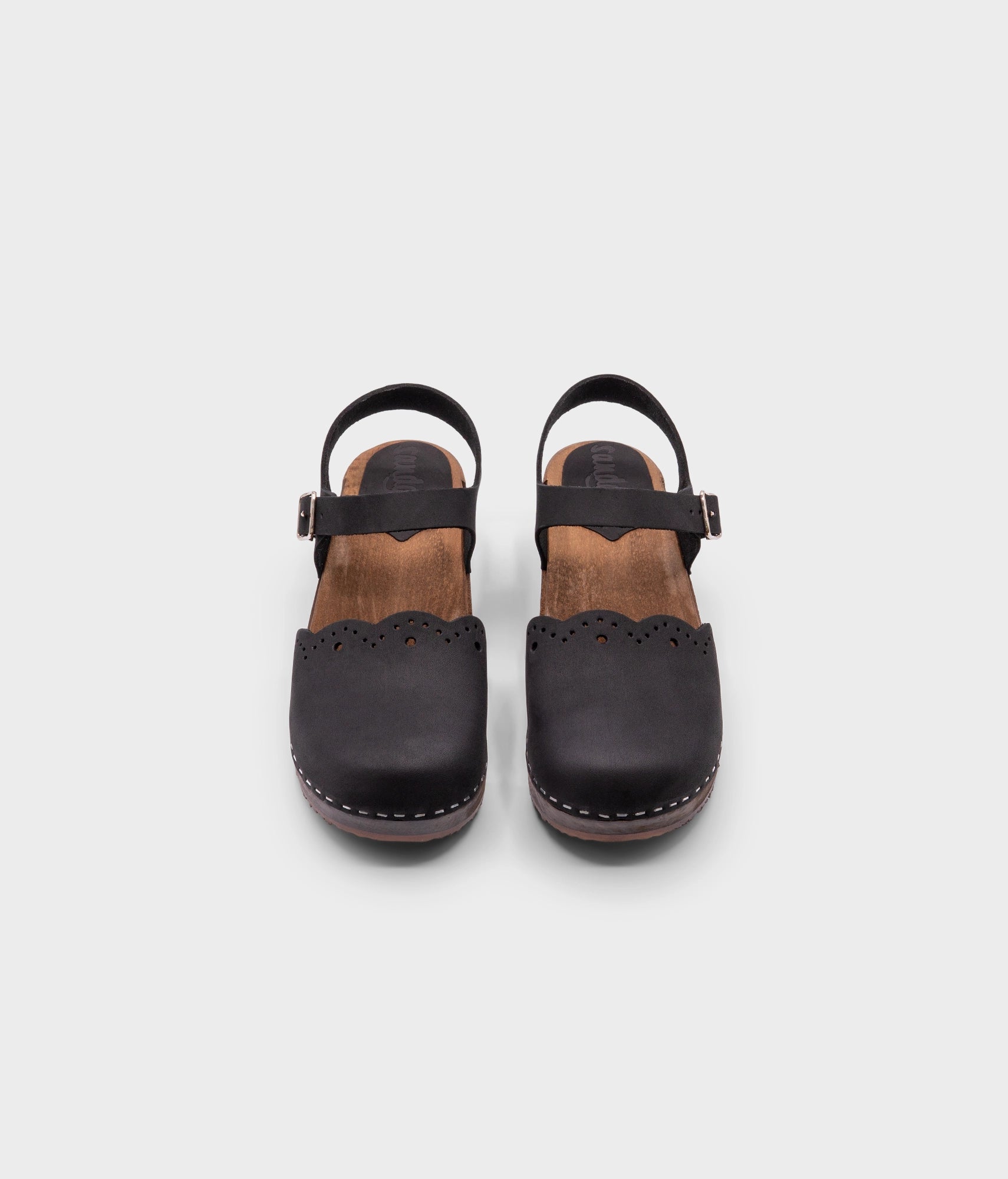 low heeled closed-toe clog sandals in black nubuck leather with a wavy leather cutout stapled on a dark wooden base
