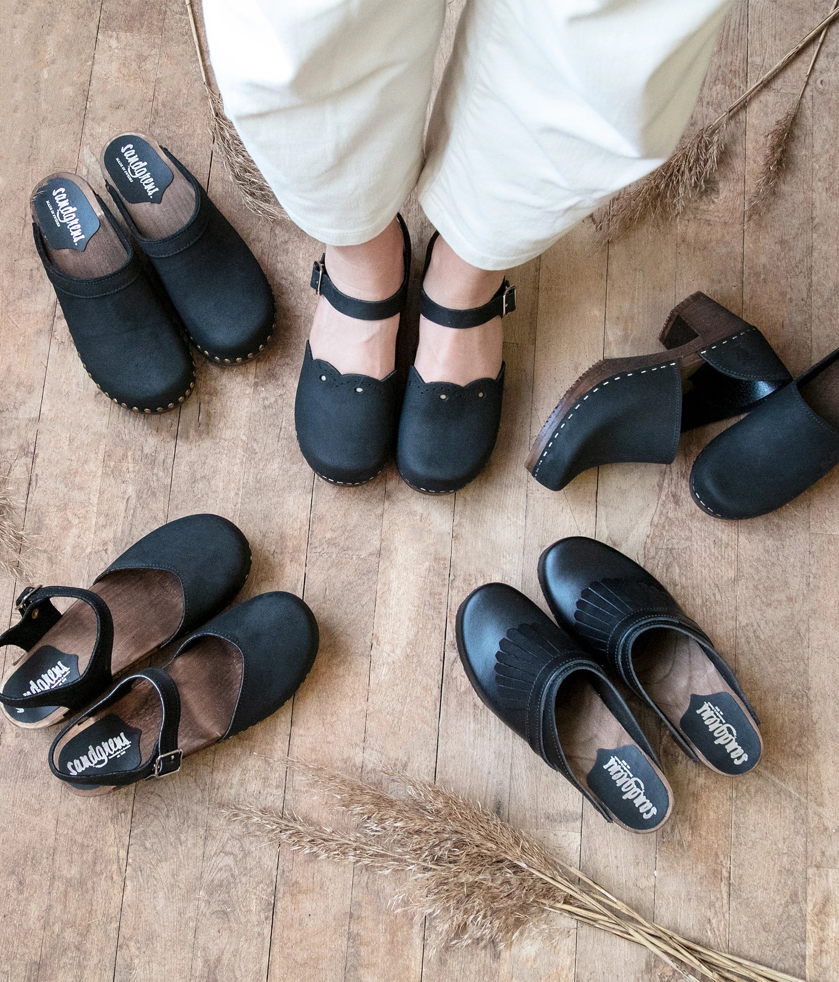 low heeled closed-toe clog sandals in black nubuck leather with a wavy leather cutout stapled on a dark wooden base