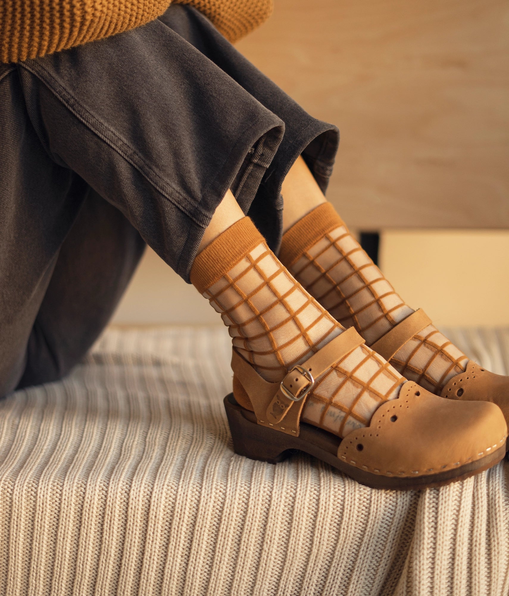 low heeled closed-toe clog sandals in light brown nubuck leather with a wavy leather cutout stapled on a dark wooden base