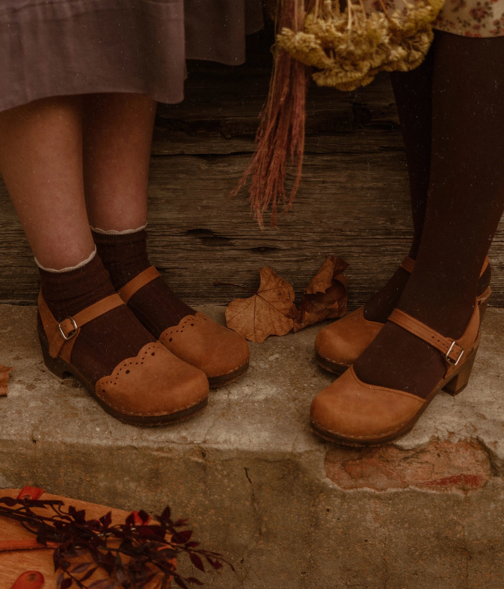 low heeled closed-toe clog sandals in light brown nubuck leather with a wavy leather cutout stapled on a dark wooden base