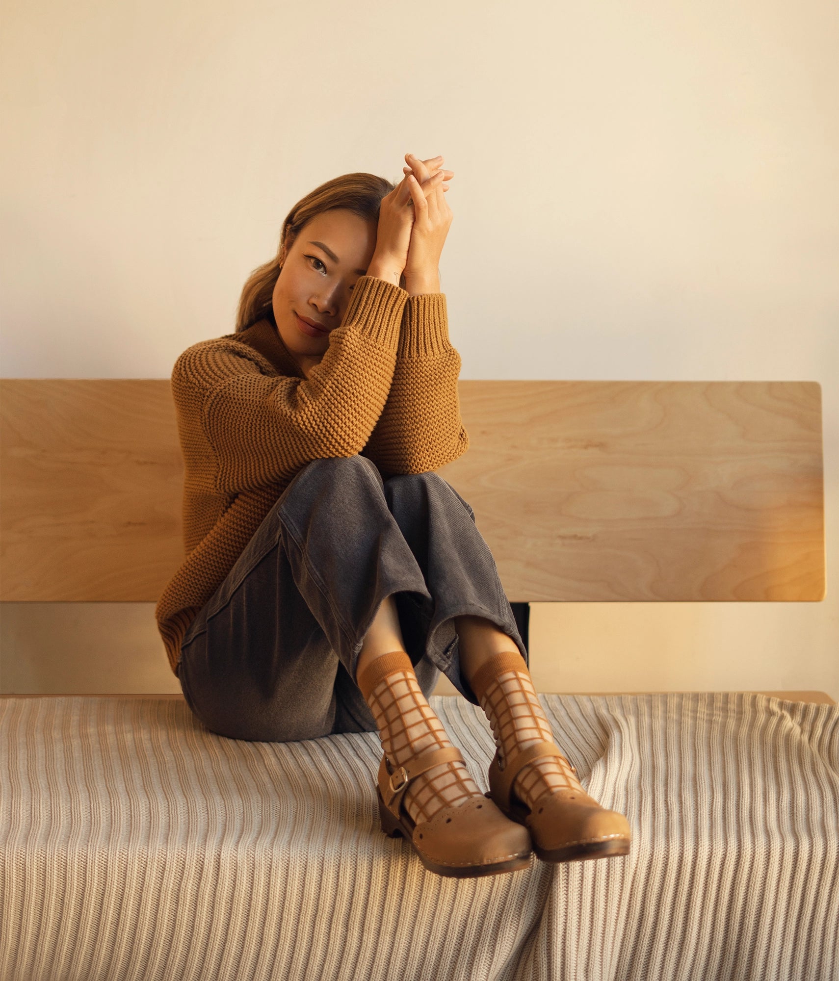low heeled closed-toe clog sandals in light brown nubuck leather with a wavy leather cutout stapled on a dark wooden base