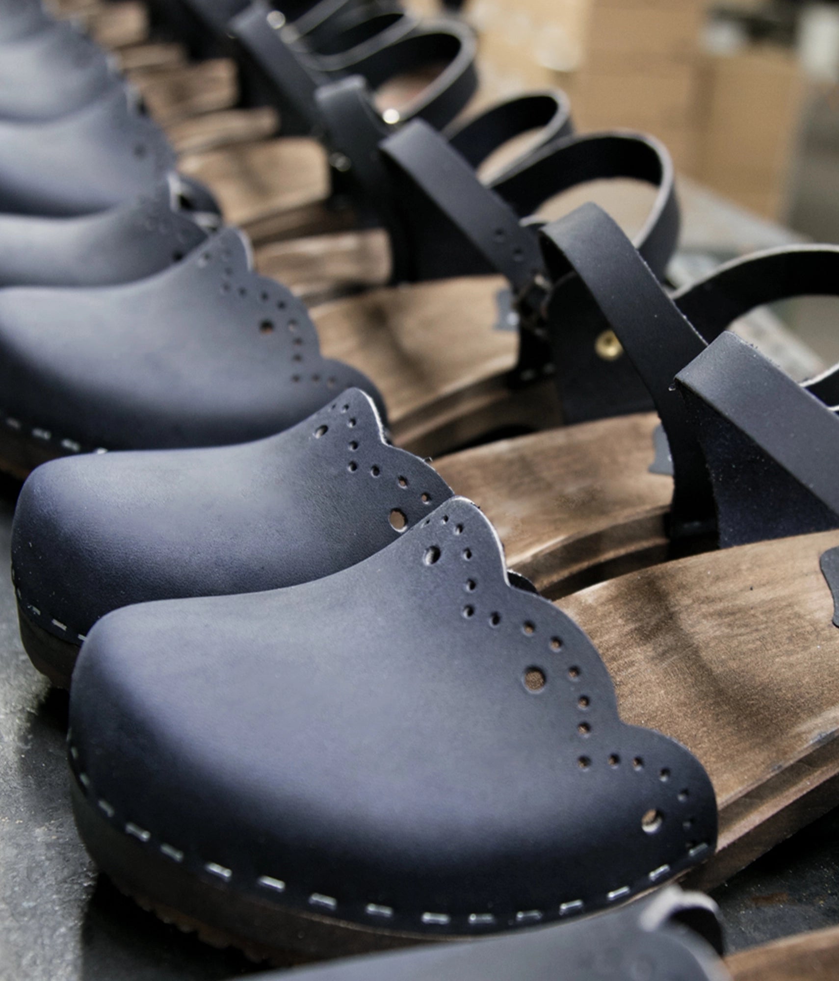 low heeled closed-toe clog sandals in navy blue nubuck leather with a wavy leather cutout stapled on a dark wooden base