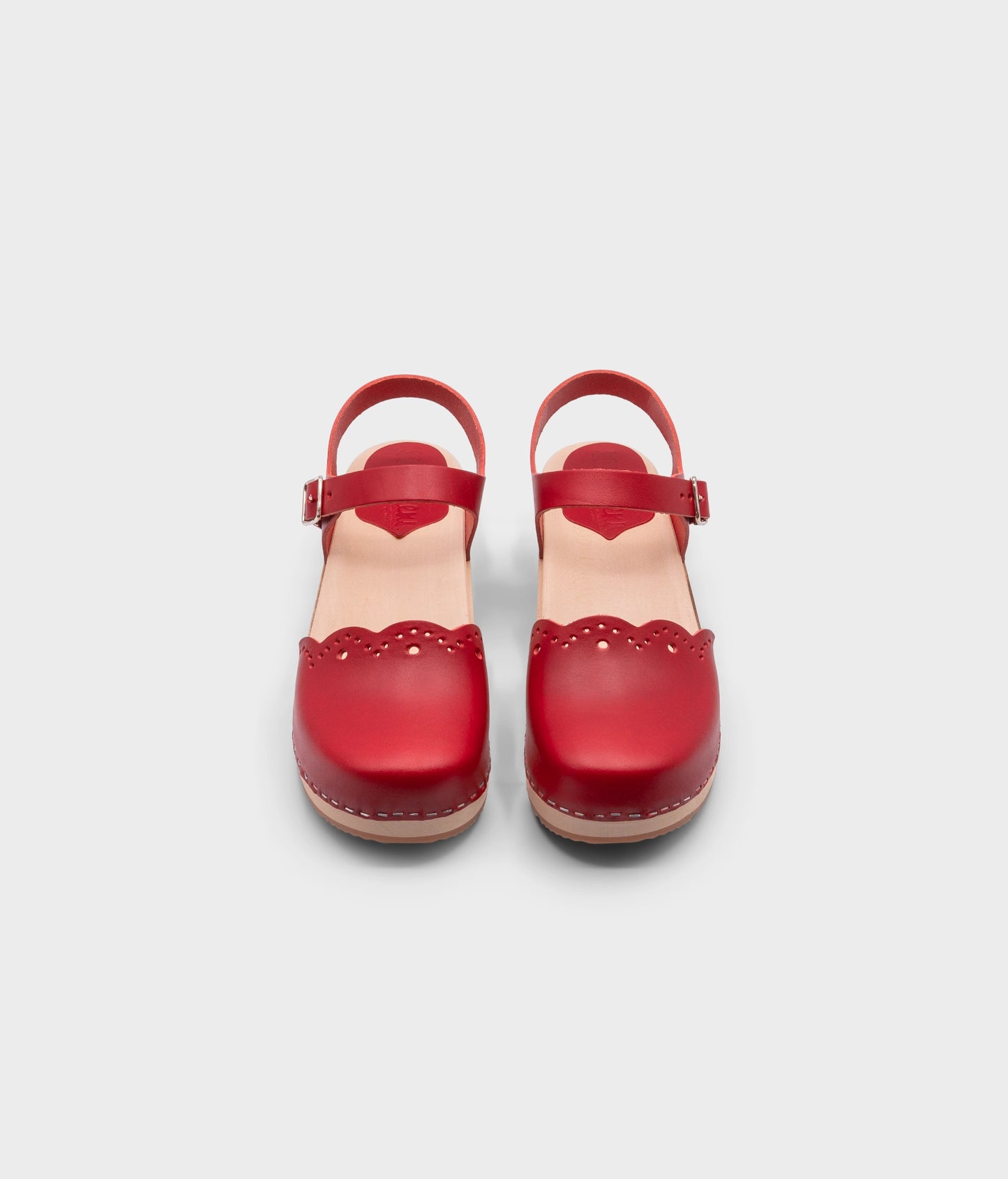low heeled closed-toe clog sandals in red vegetable tanned leather with a wavy leather cutout stapled on a light wooden base