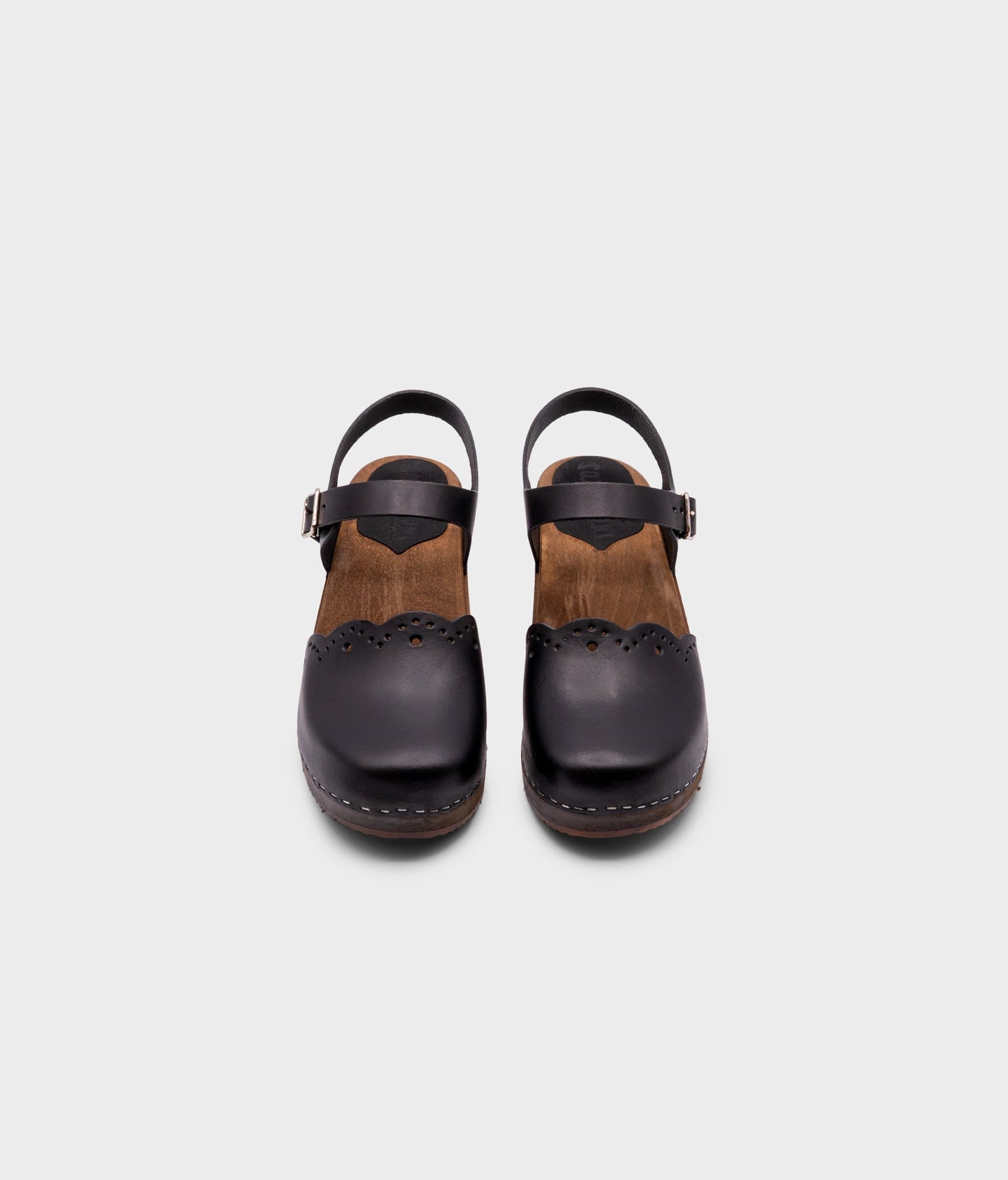 low heeled closed-toe clog sandals in black vegetable tanned leather with a wavy leather cutout stapled on a dark wooden base