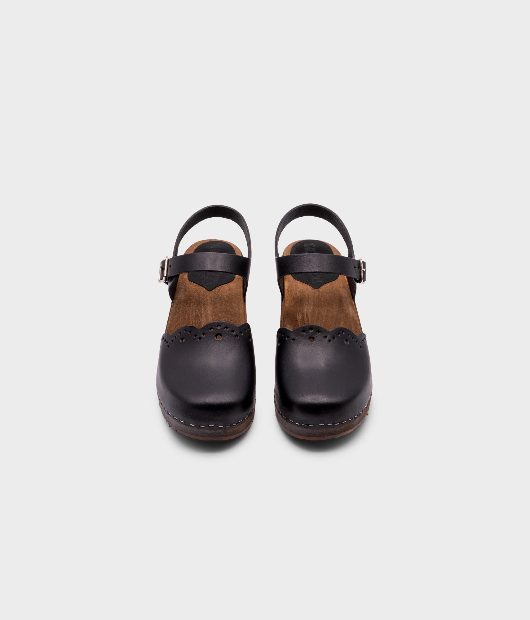 low heeled closed-toe clog sandals in black vegetable tanned leather with a wavy leather cutout stapled on a dark wooden base
