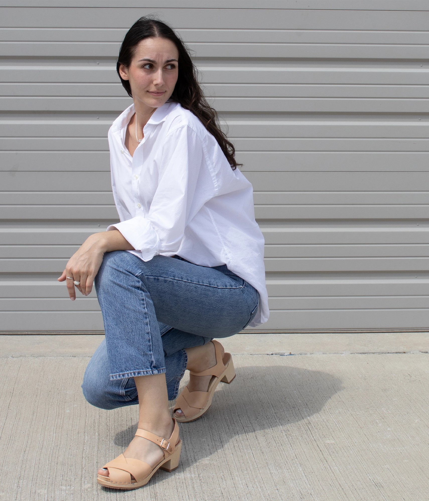 Woman wearing high heeled clog sandals in ecru beige vegetable tanned leather with an open-toe stapled on a light wooden base