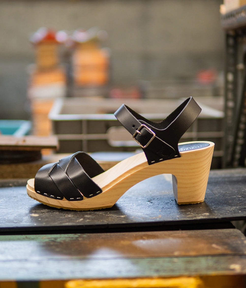 High rise heel clog sandals in black vegetable tanned leather stapled on a light wooden base with an open toe