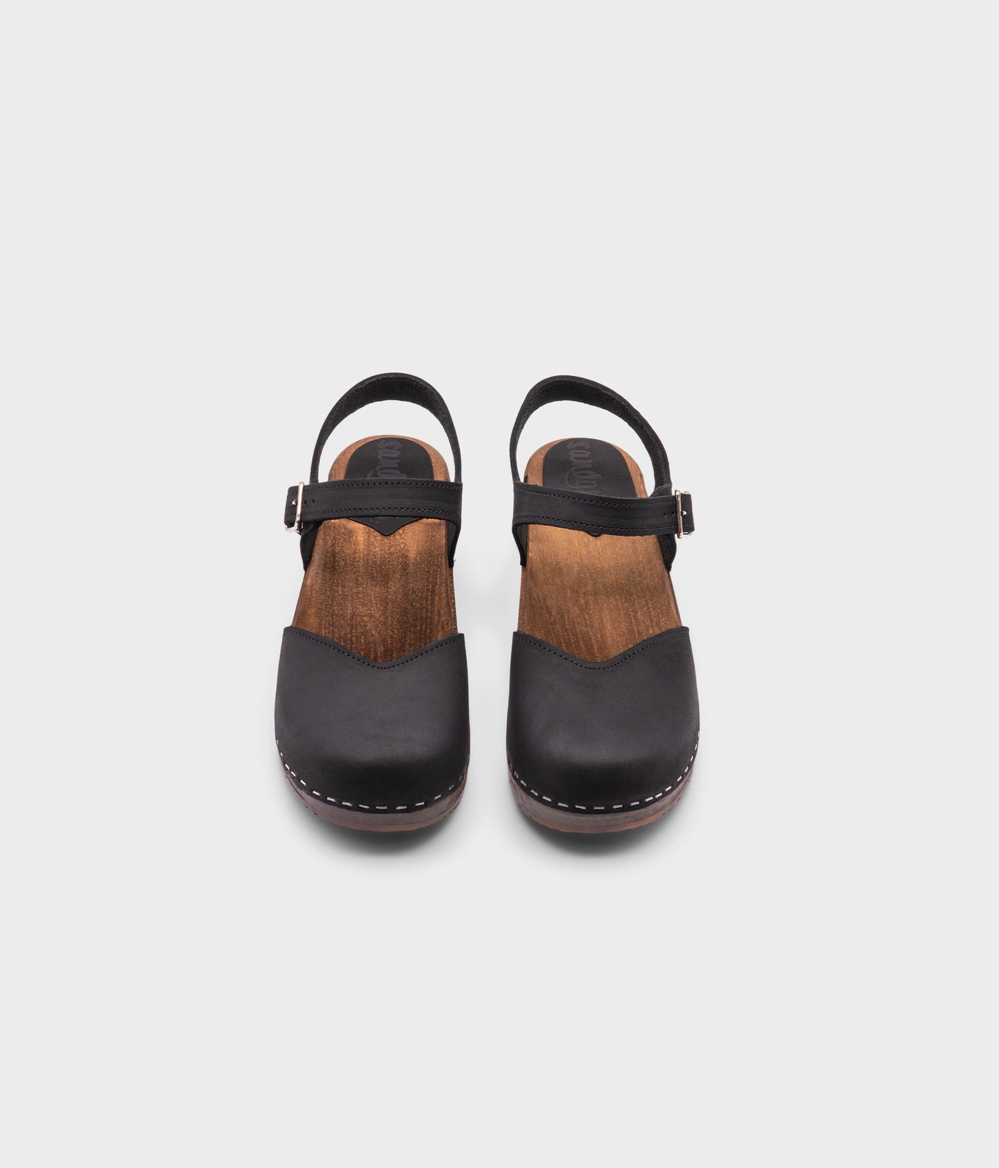 classic low heeled closed-toe sandal in black nubuck leather stapled on a dark wooden base