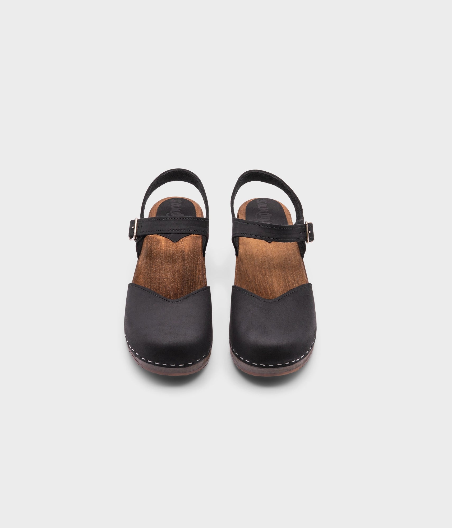 classic low heeled closed-toe sandal in black nubuck leather stapled on a dark wooden base