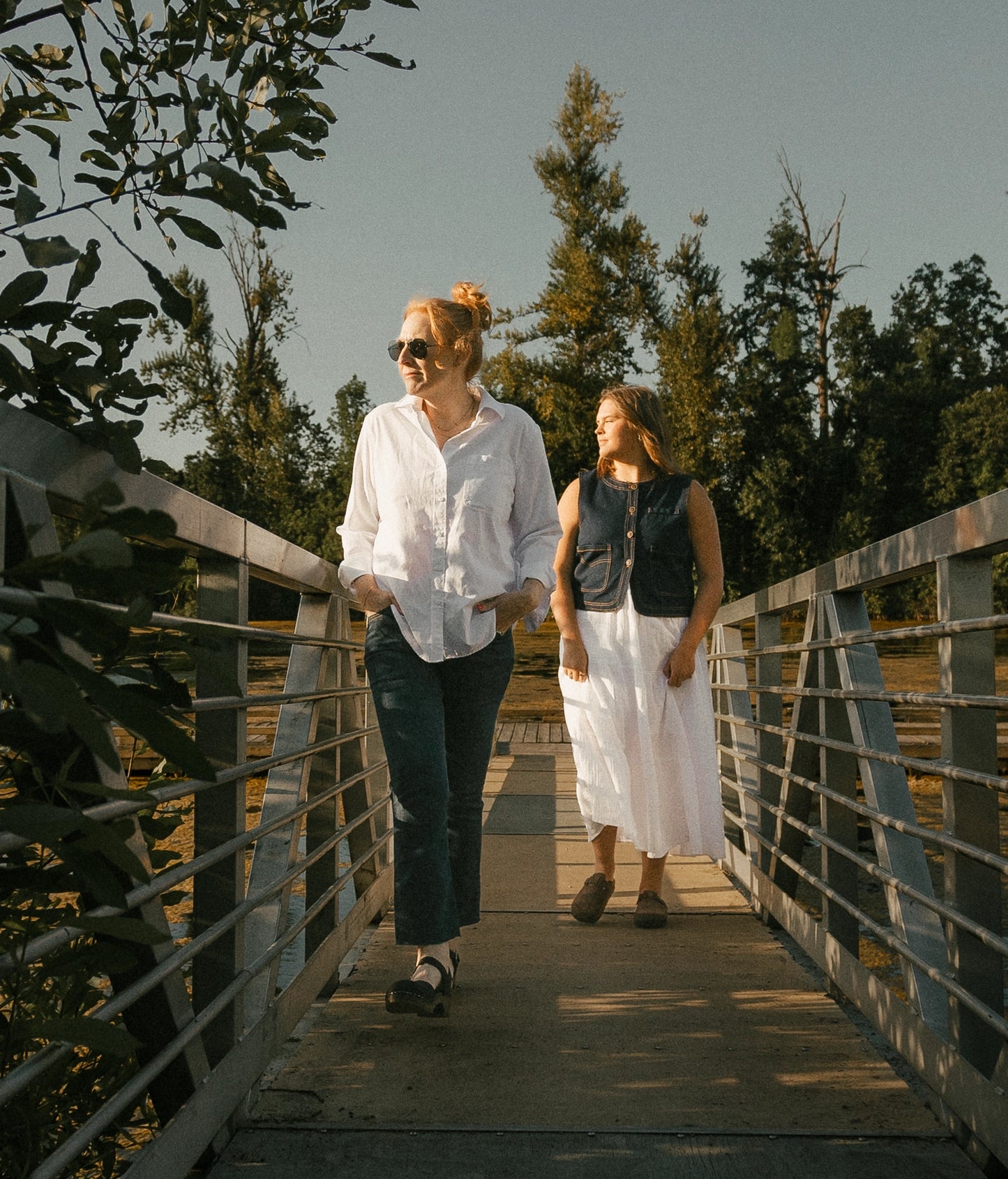 Two women walking in Sandgrens footwear. Classic low heeled closed-toe sandal in black nubuck leather stapled on a dark wooden base