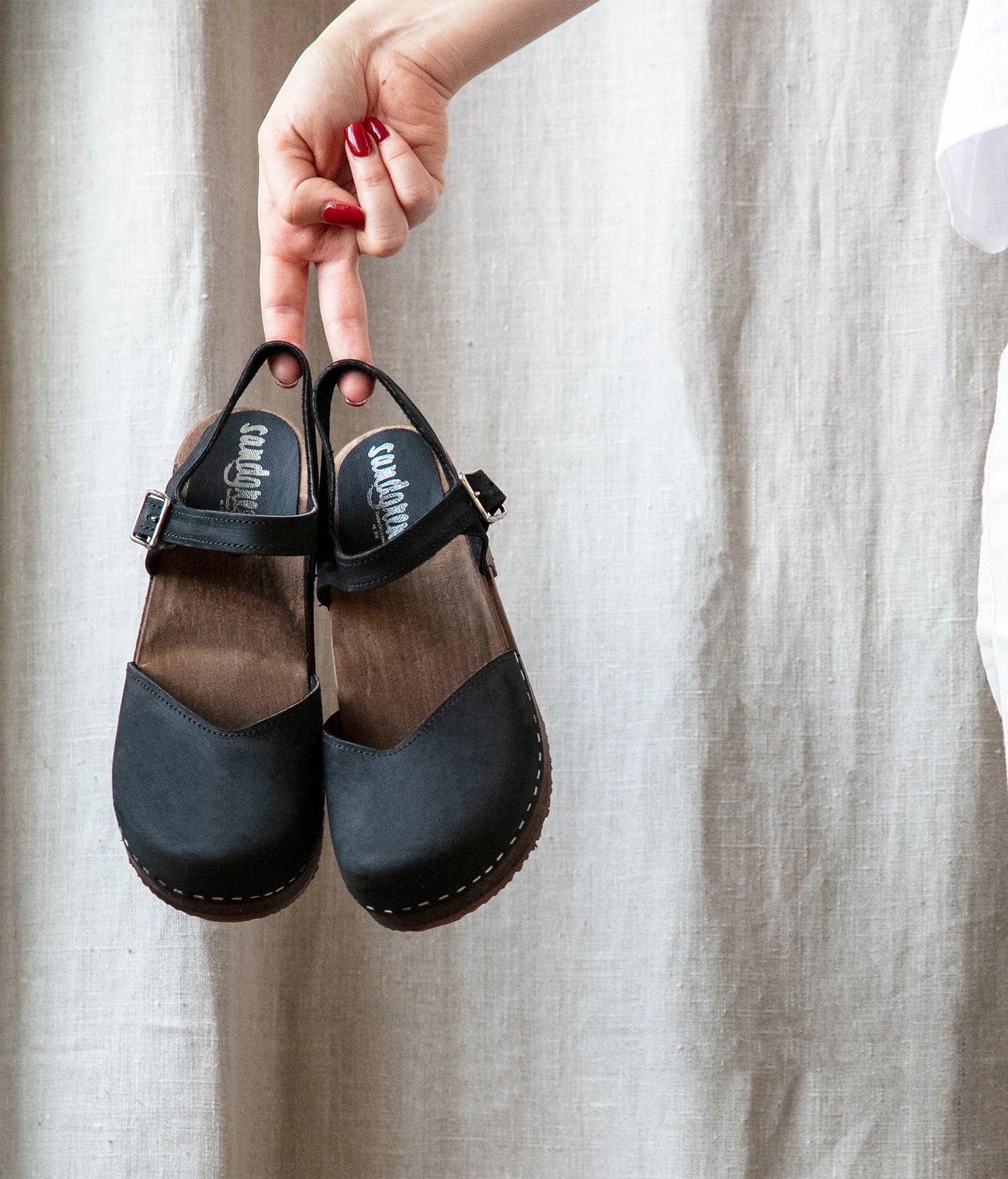 classic low heeled closed-toe sandal in black nubuck leather stapled on a dark wooden base