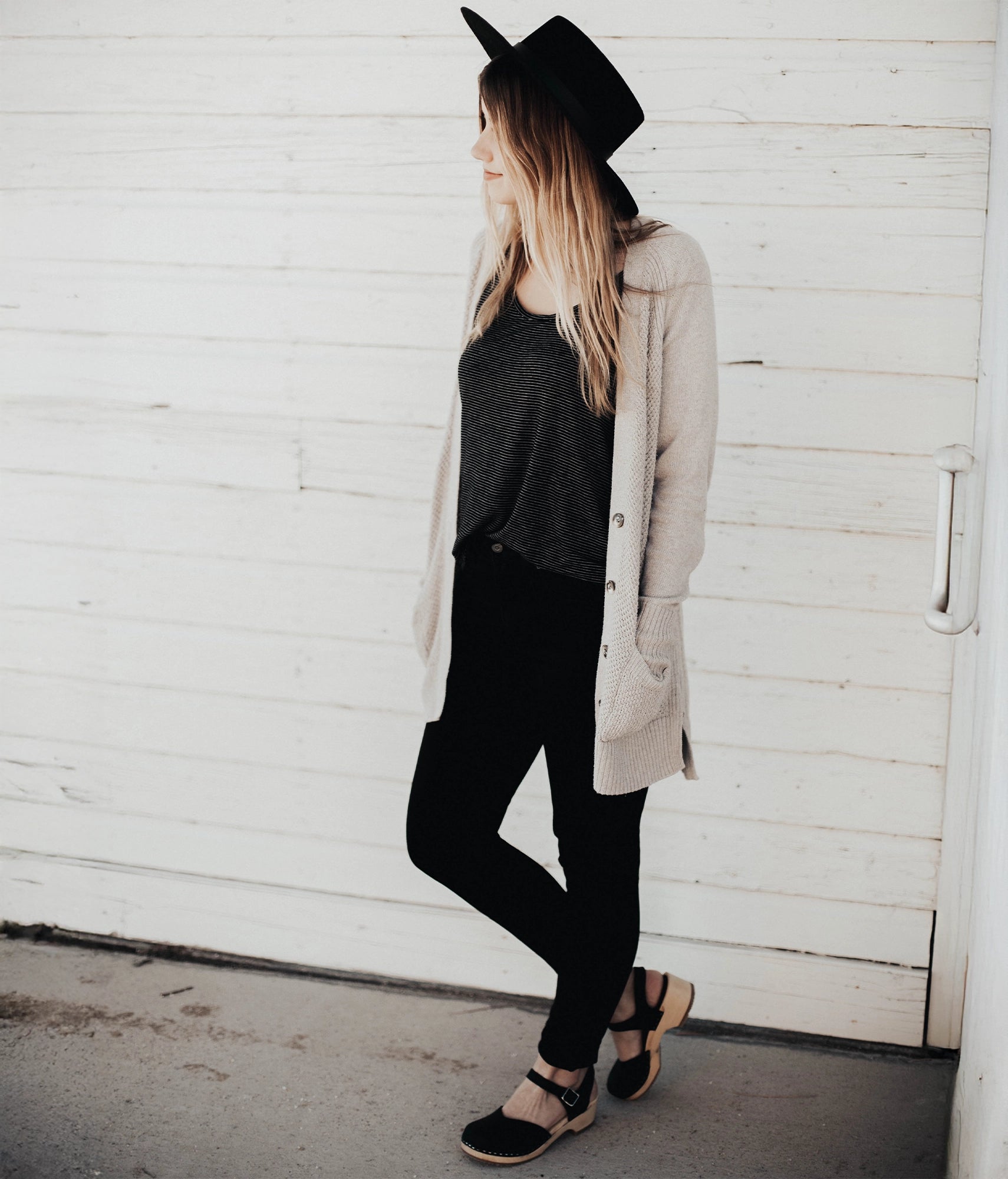 women wearing classic low heeled closed-toe sandal in black nubuck leather stapled on a light wooden base