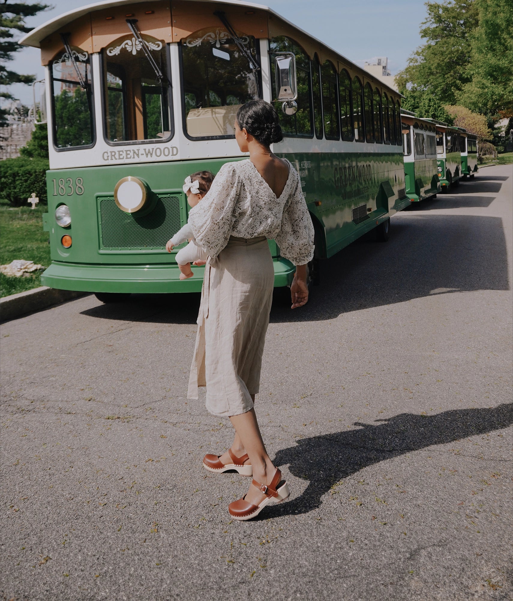 woman wearing a linen skirt and flowered blouse with classic low heeled closed-toe sandal in cognac red vegetable tanned leather stapled on a light wooden base
