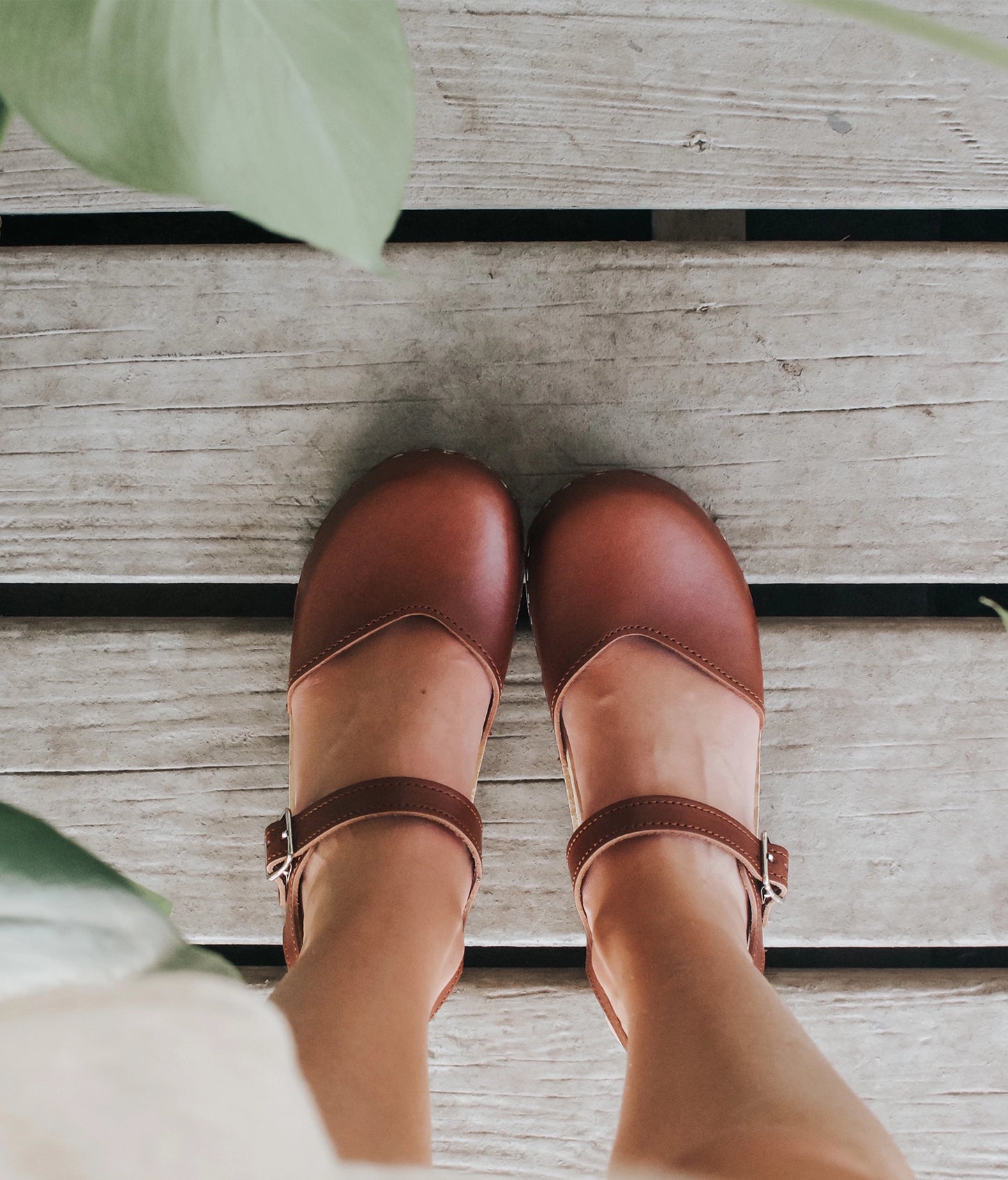 Women wearing classic low heeled closed-toe sandal in cognac red vegetable tanned leather stapled on a light wooden base