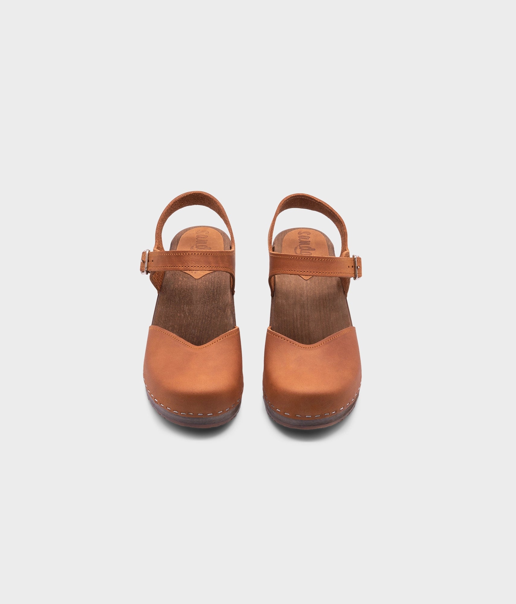 classic low heeled closed-toe sandal in light brown nubuck leather stapled on a dark wooden base